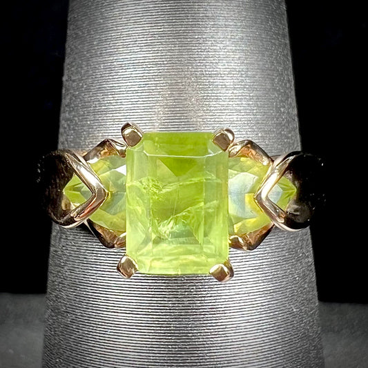A ladies' three stone peridot ring in yellow gold.  The center stone is emerald cut, and the side stones are pear shaped.