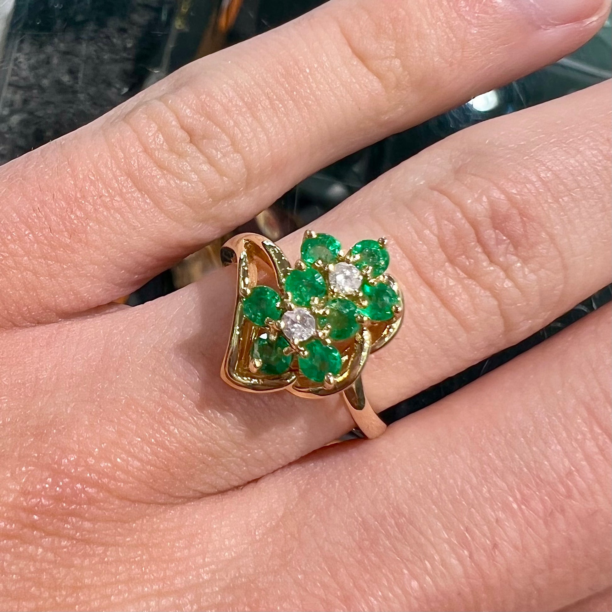 A yellow gold ring set with round cut emerald and diamonds that form the shape of two flowers.
