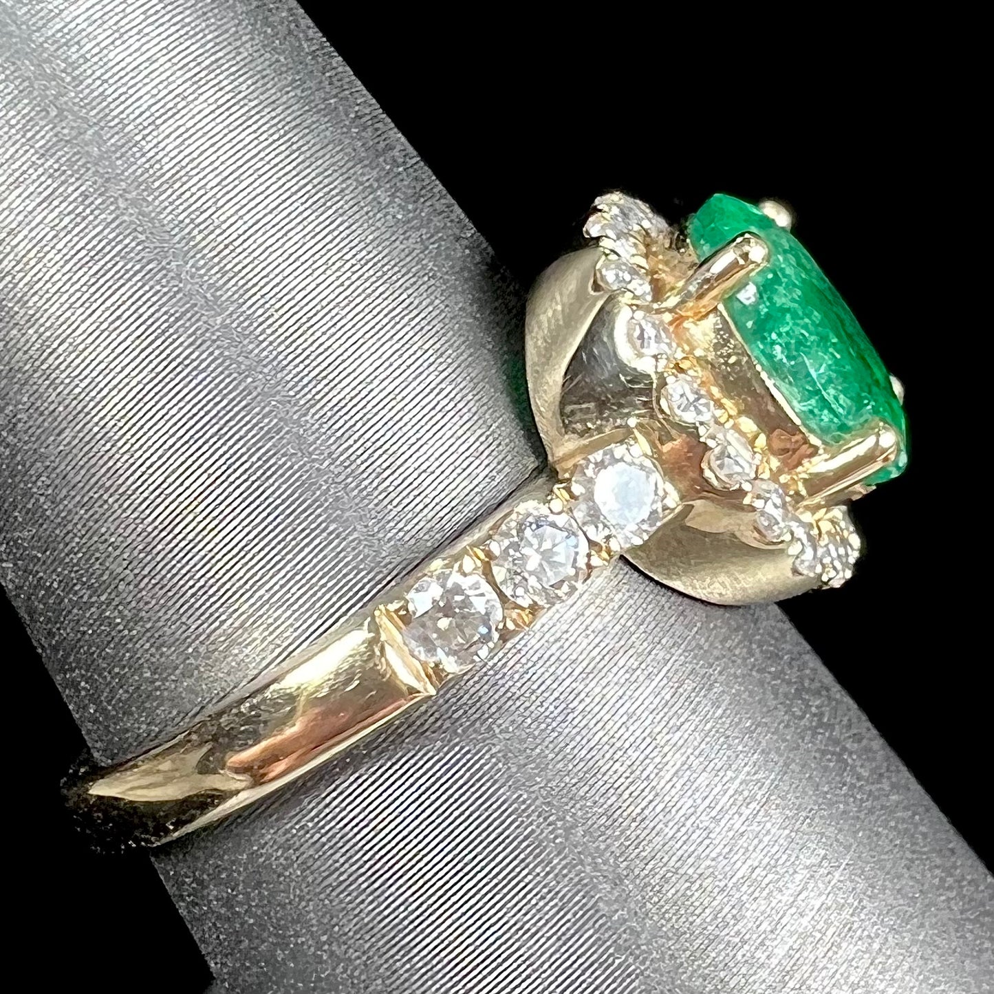 A ladies' yellow gold ring set with an oval cut emerald in a halo of diamonds. 