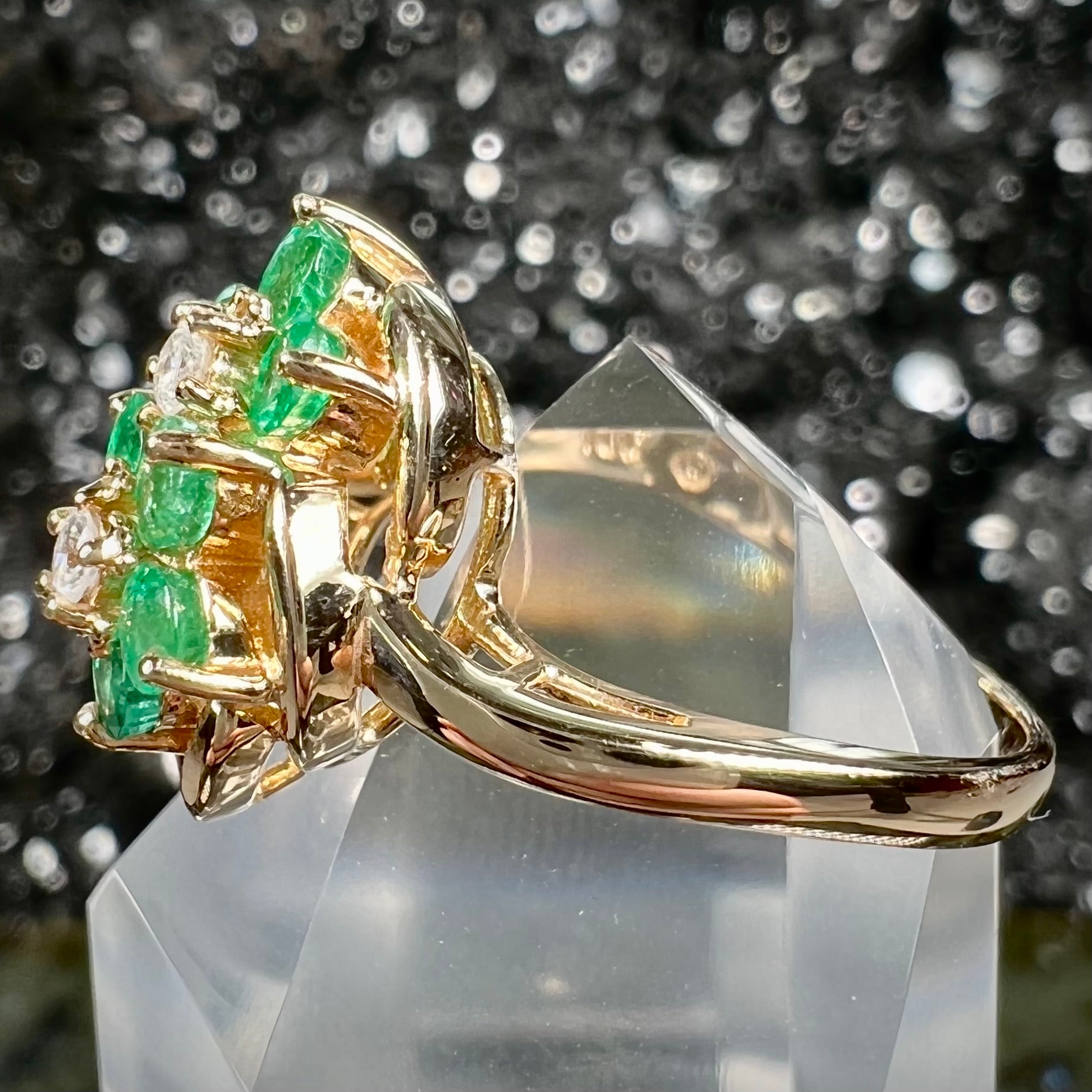 A yellow gold ring set with round cut emerald and diamonds that form the shape of two flowers.