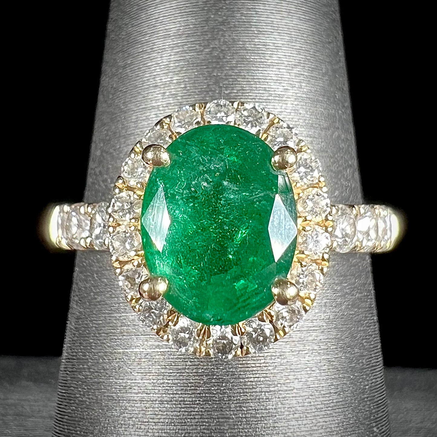 A ladies' yellow gold ring set with an oval cut emerald in a halo of diamonds. 