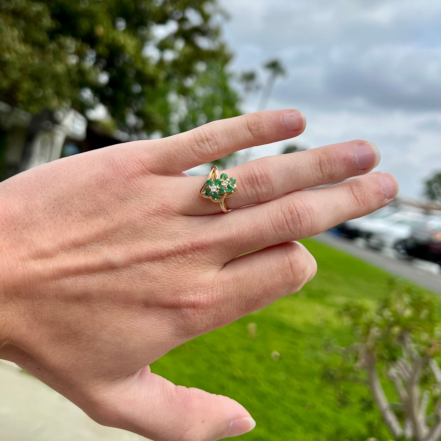 A yellow gold ring set with round cut emerald and diamonds that form the shape of two flowers.