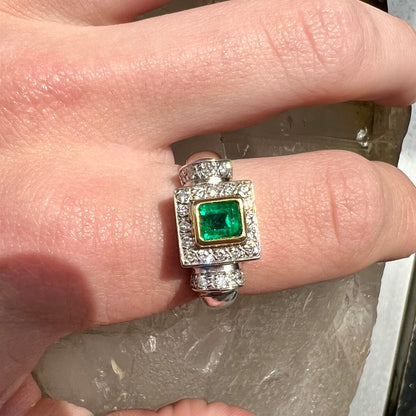 A two tone gold emerald and diamond halo ring.