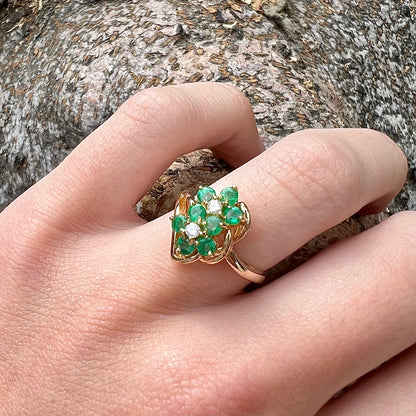 A yellow gold ring set with round cut emerald and diamonds that form the shape of two flowers.