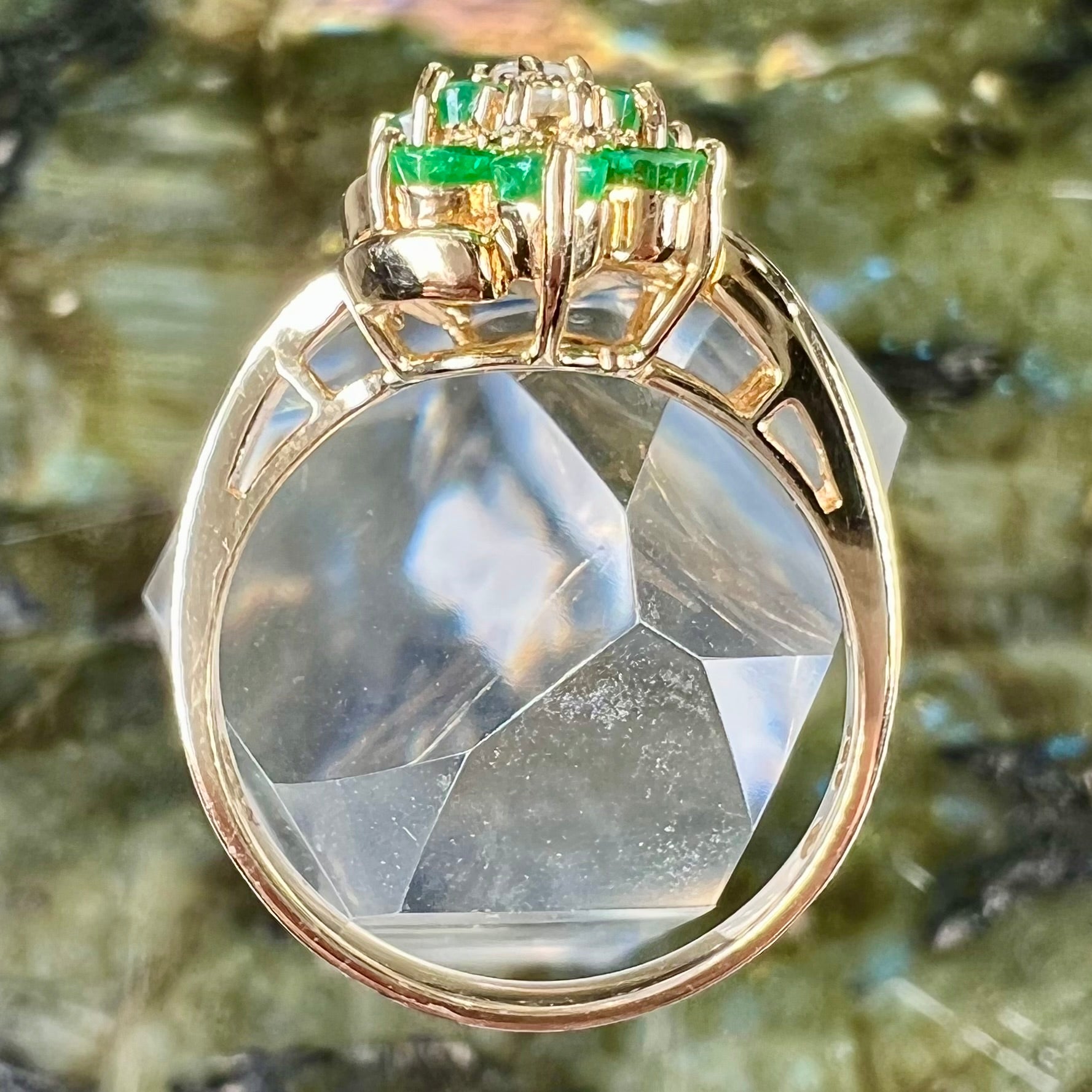 A yellow gold ring set with round cut emerald and diamonds that form the shape of two flowers.