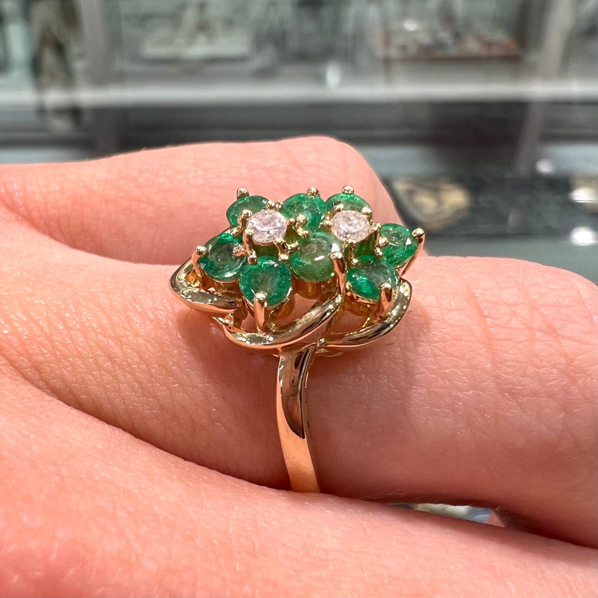 A yellow gold ring set with round cut emerald and diamonds that form the shape of two flowers.