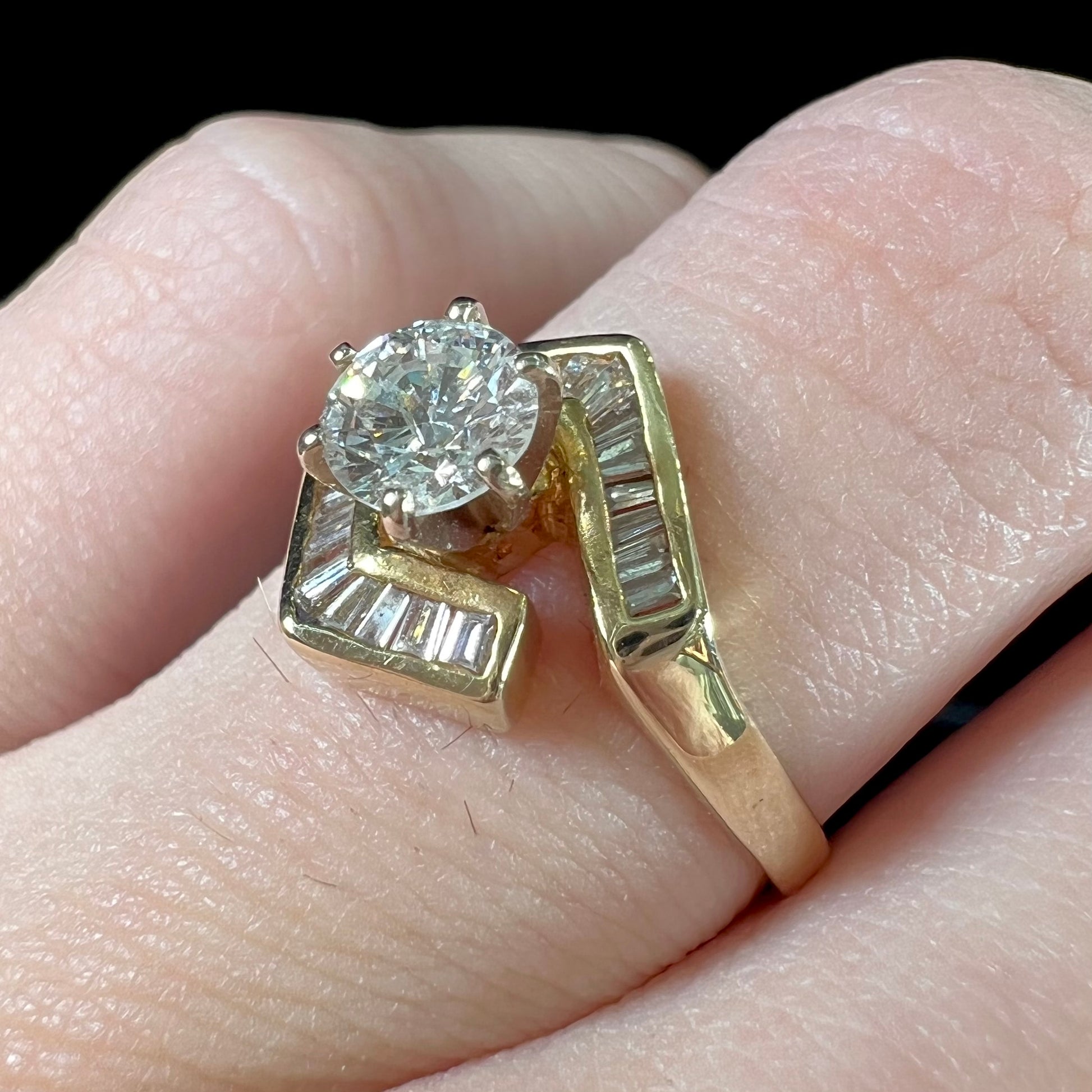 A gold diamond ring set with a round cut center stone with channel set baguette cut accent stones.