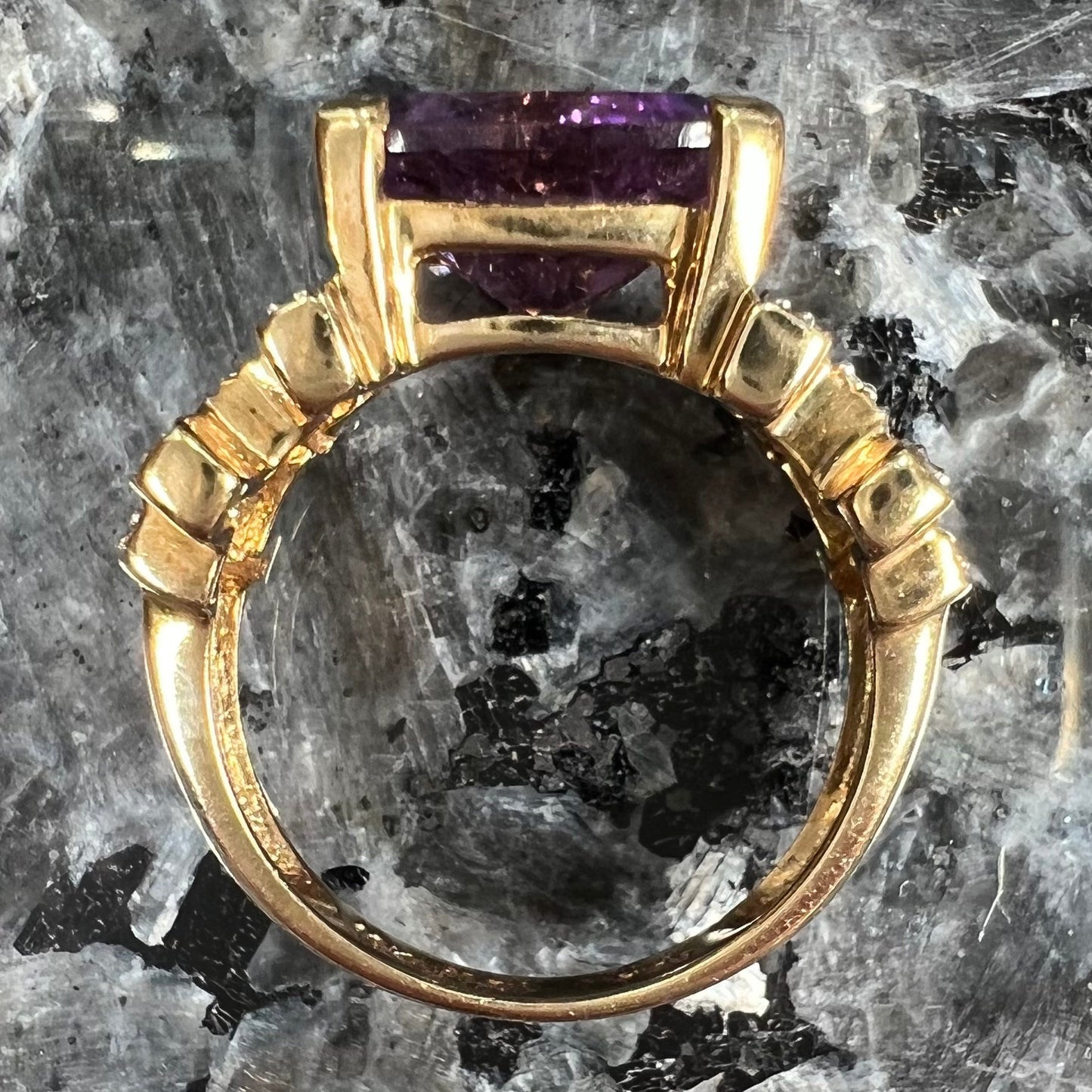 A yellow gold ring set with a trillion cut amethyst and round diamond accent stones.