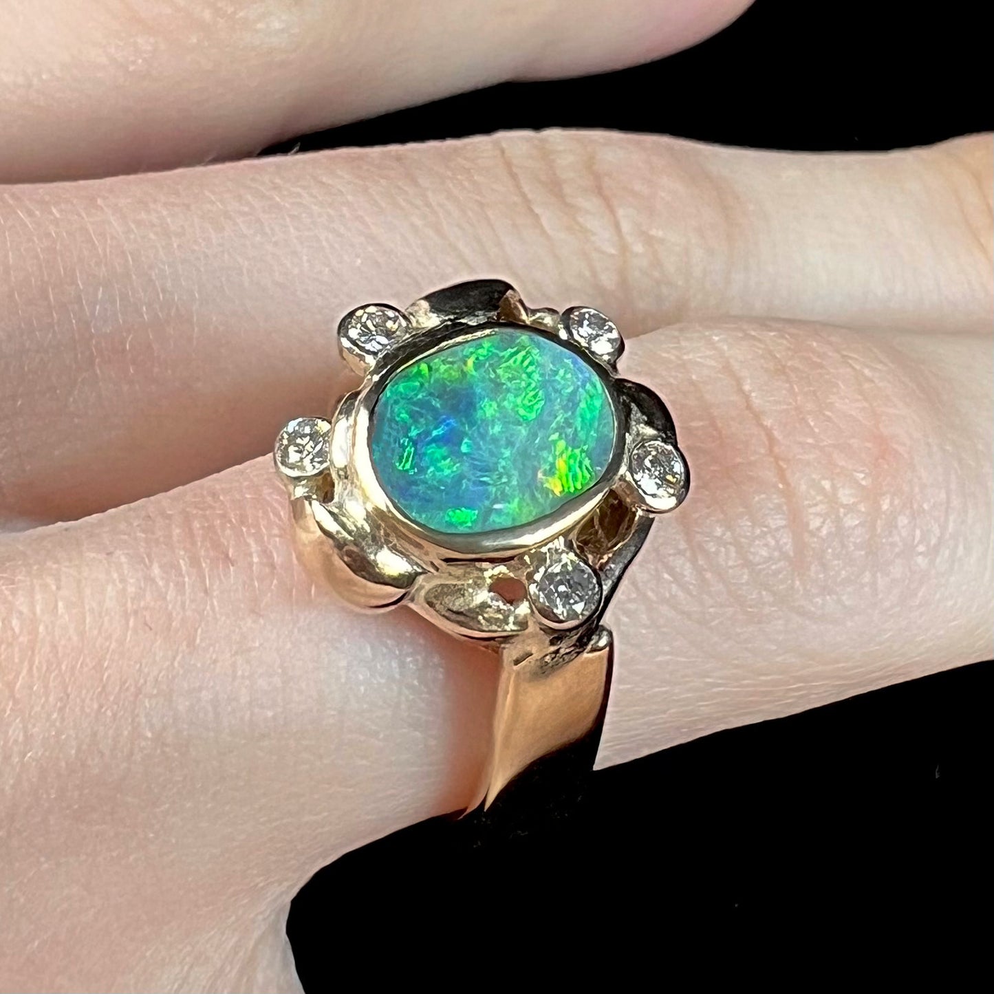 A ladies' yellow gold oval cut natural black opal ring set with five round accent diamonds.