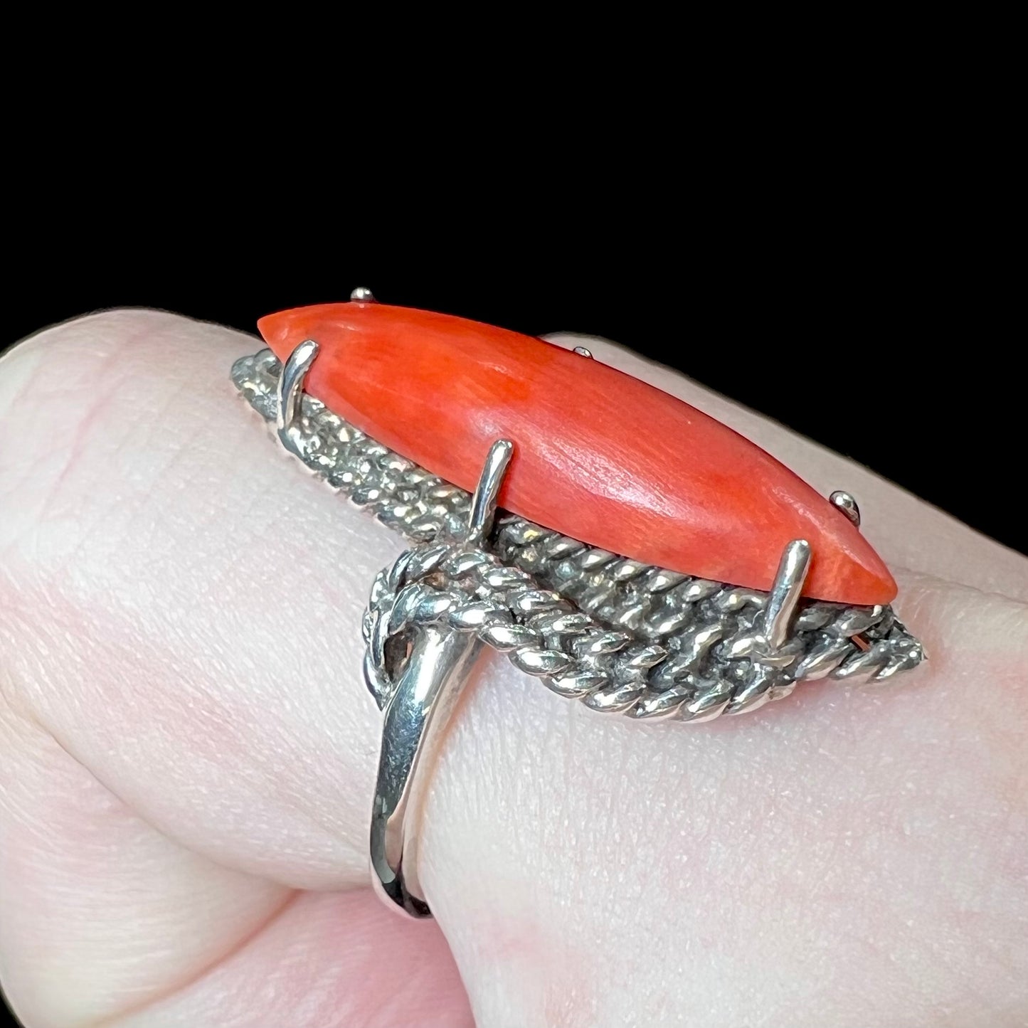 A prong-set silver ring set with a red marquise cut coral.