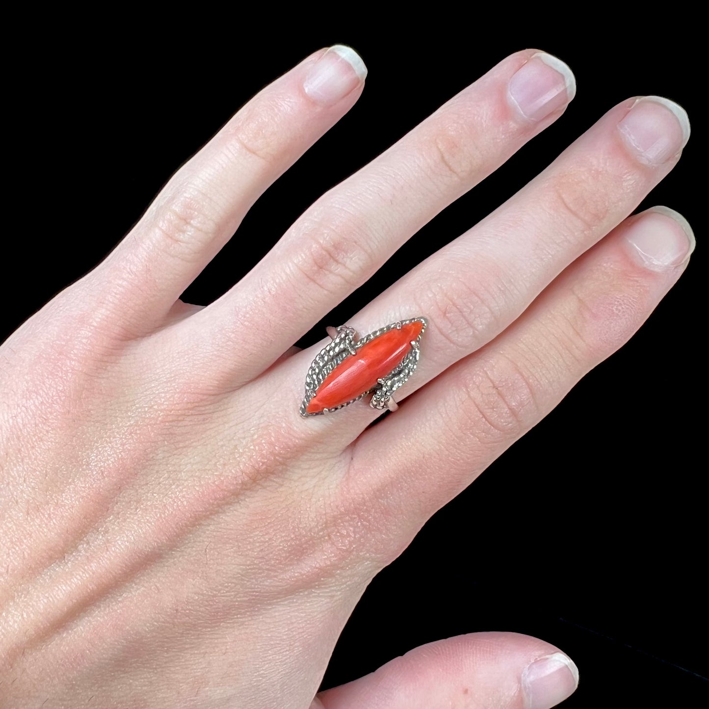 A prong-set silver ring set with a red marquise cut coral.