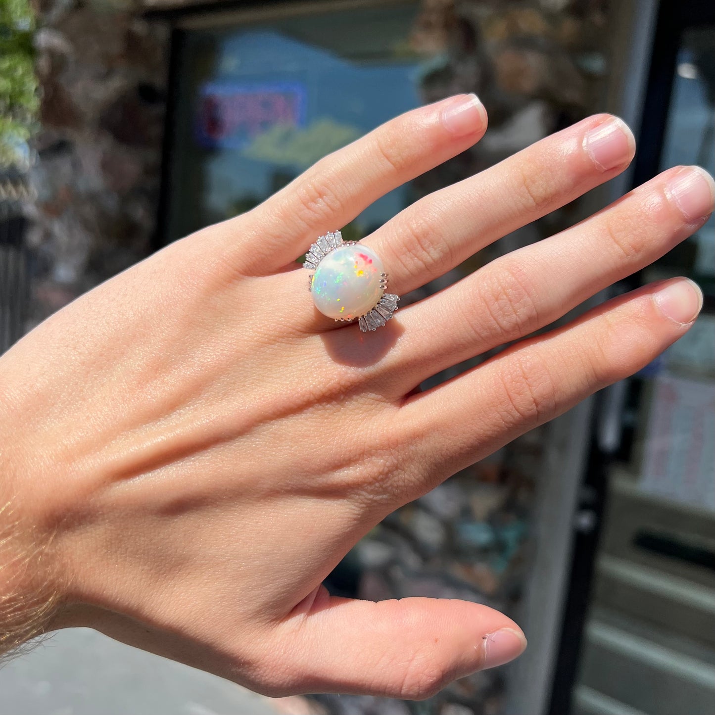 An oval cabochon cut opal mounted in a ladies' white gold ring between tapered baguette cut diamonds.