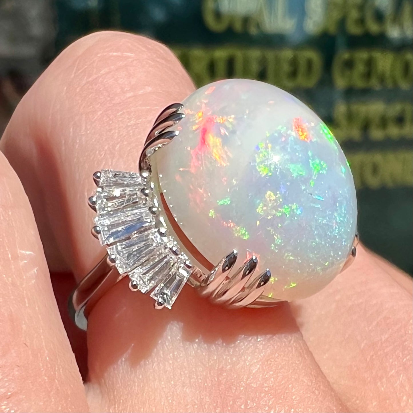 An oval cabochon cut opal mounted in a ladies' white gold ring between tapered baguette cut diamonds.