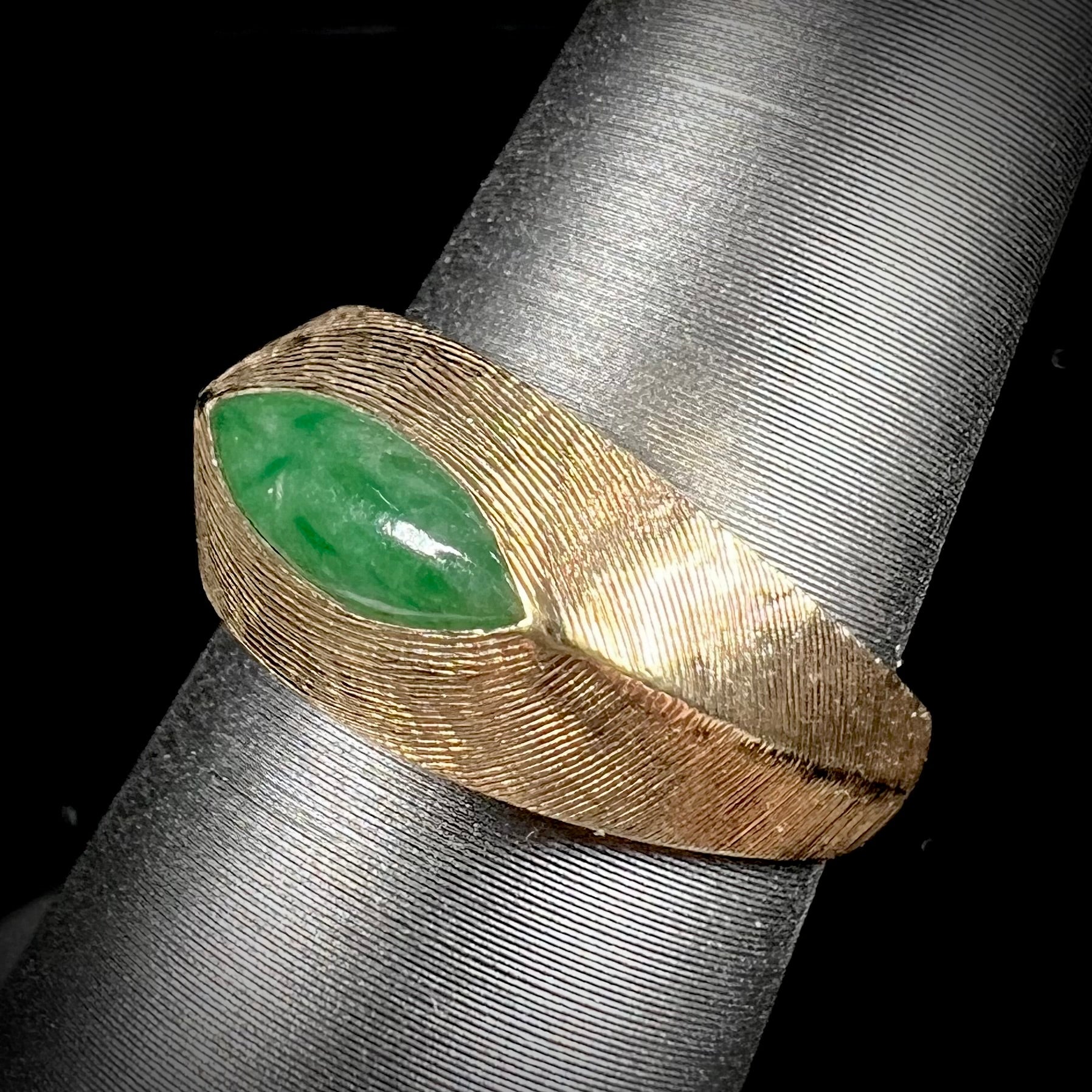 A textured yellow gold ring set with a marquise cabochon cut green jadeite stone.