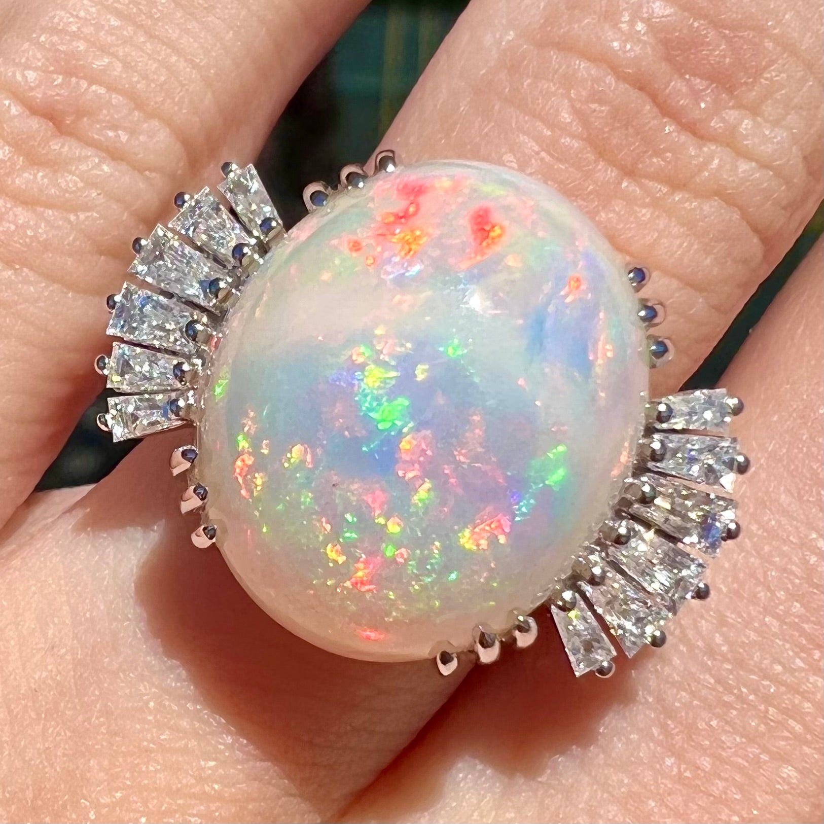 An oval cabochon cut opal mounted in a ladies' white gold ring between tapered baguette cut diamonds.