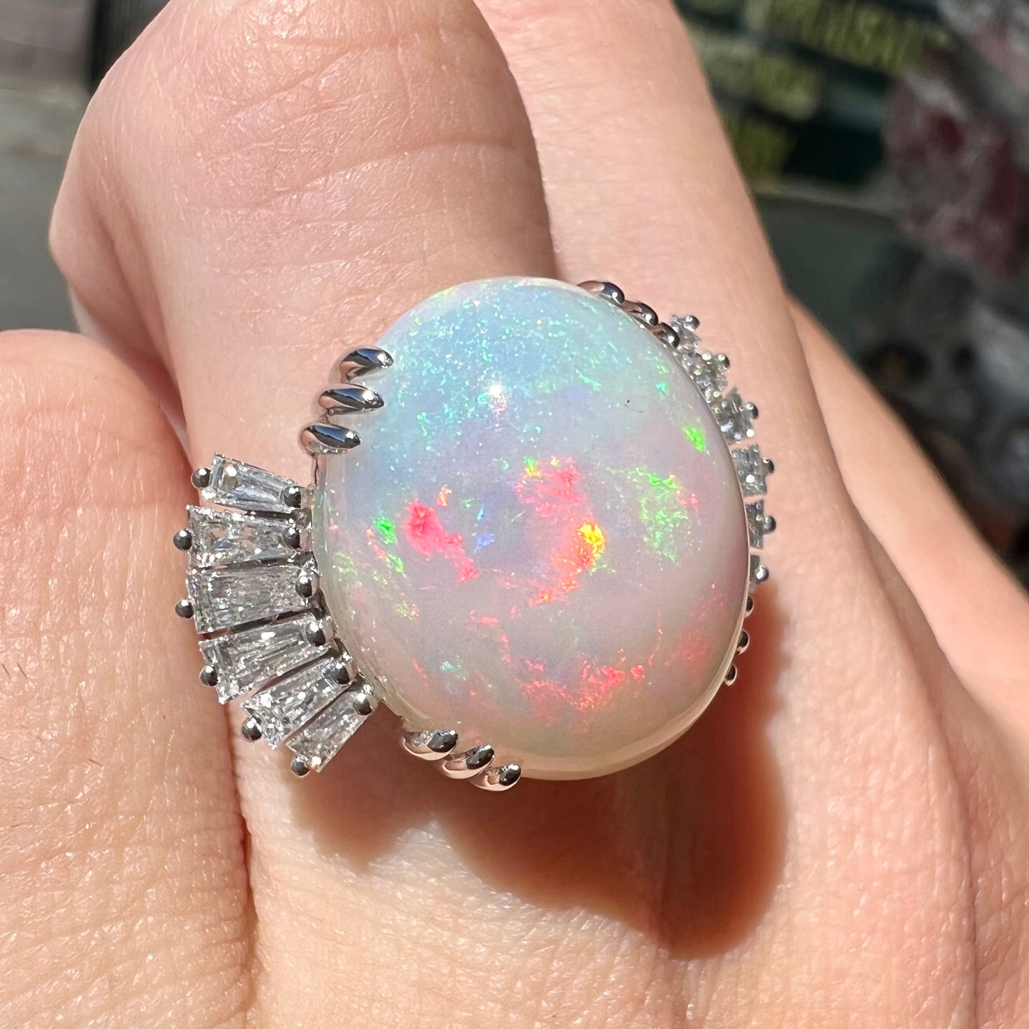 An oval cabochon cut opal mounted in a ladies' white gold ring between tapered baguette cut diamonds.