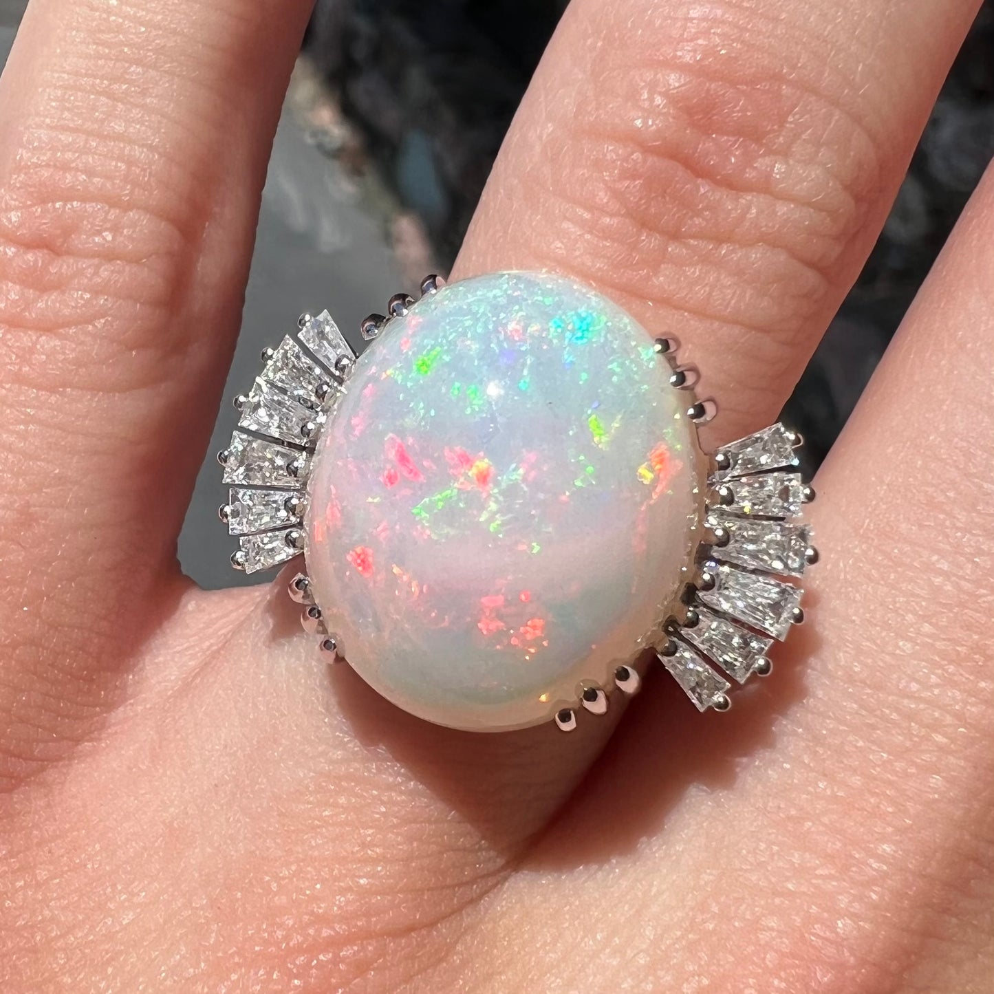 An oval cabochon cut opal mounted in a ladies' white gold ring between tapered baguette cut diamonds.