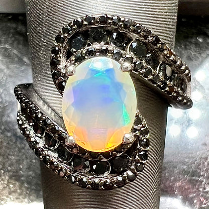A sterling silver ring set with round black spinel stones and an oval cut, faceted Ethiopian opal.