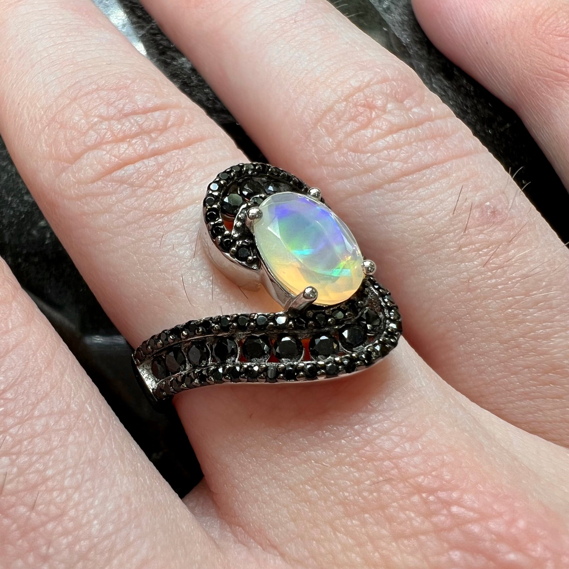 A sterling silver ring set with round black spinel stones and an oval cut, faceted Ethiopian opal.