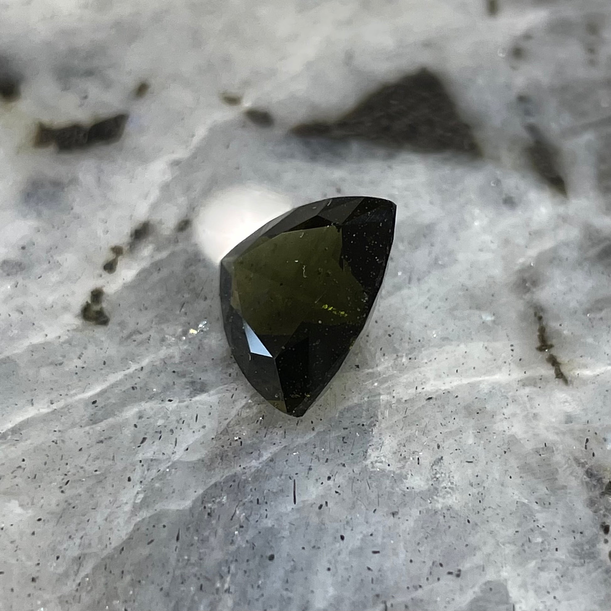 A faceted trillion cut moldavite gemstone that weighs 3.98 carats.  The stone is a dark green color.