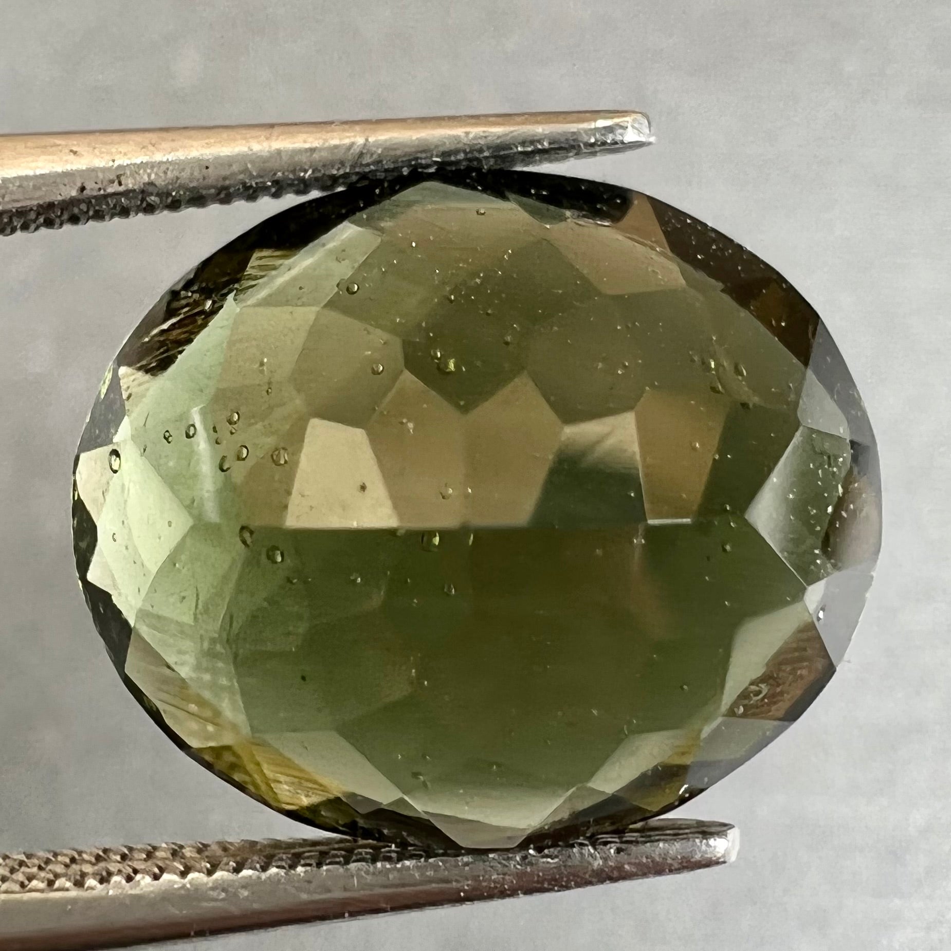 A faceted oval checkerboard cut moldavite gemstone that weighs 4.14 carats.