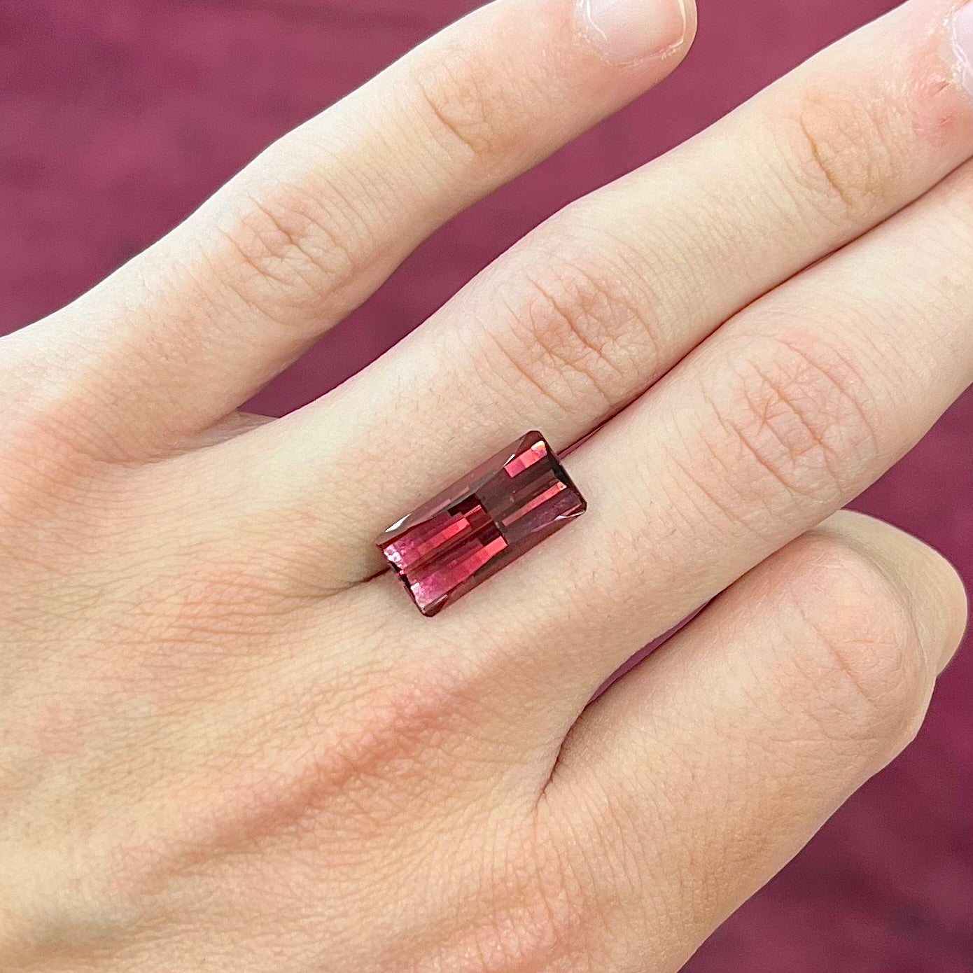 A loose, fantasy cut reddish colored tourmaline.  The cut reflects light in a way that resembles digital pixels on a screen.