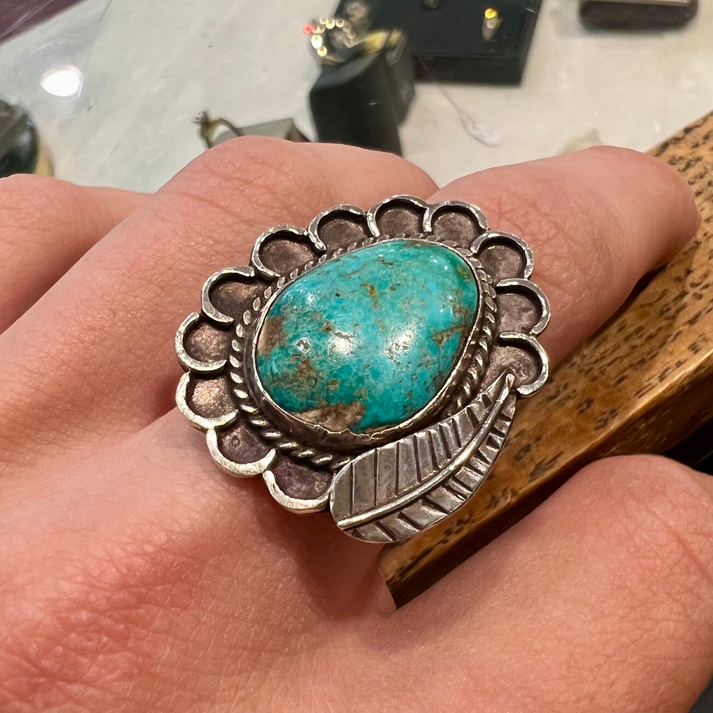 A sterling silver Navajo style ring.  The ring is set with a turquoise stone from Pilot Mountain.  There is a feather decoration next to the stone.