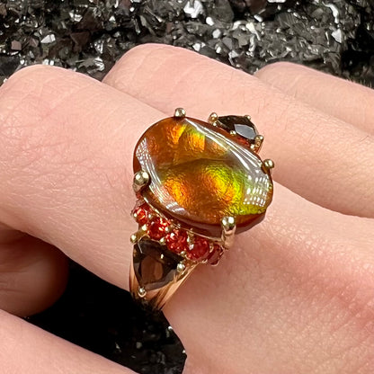 A ladies yellow gold fire agate ring set with trillion cut smoky quartz and round cut red-orange garnet accents.  The fire agate displays green and red.