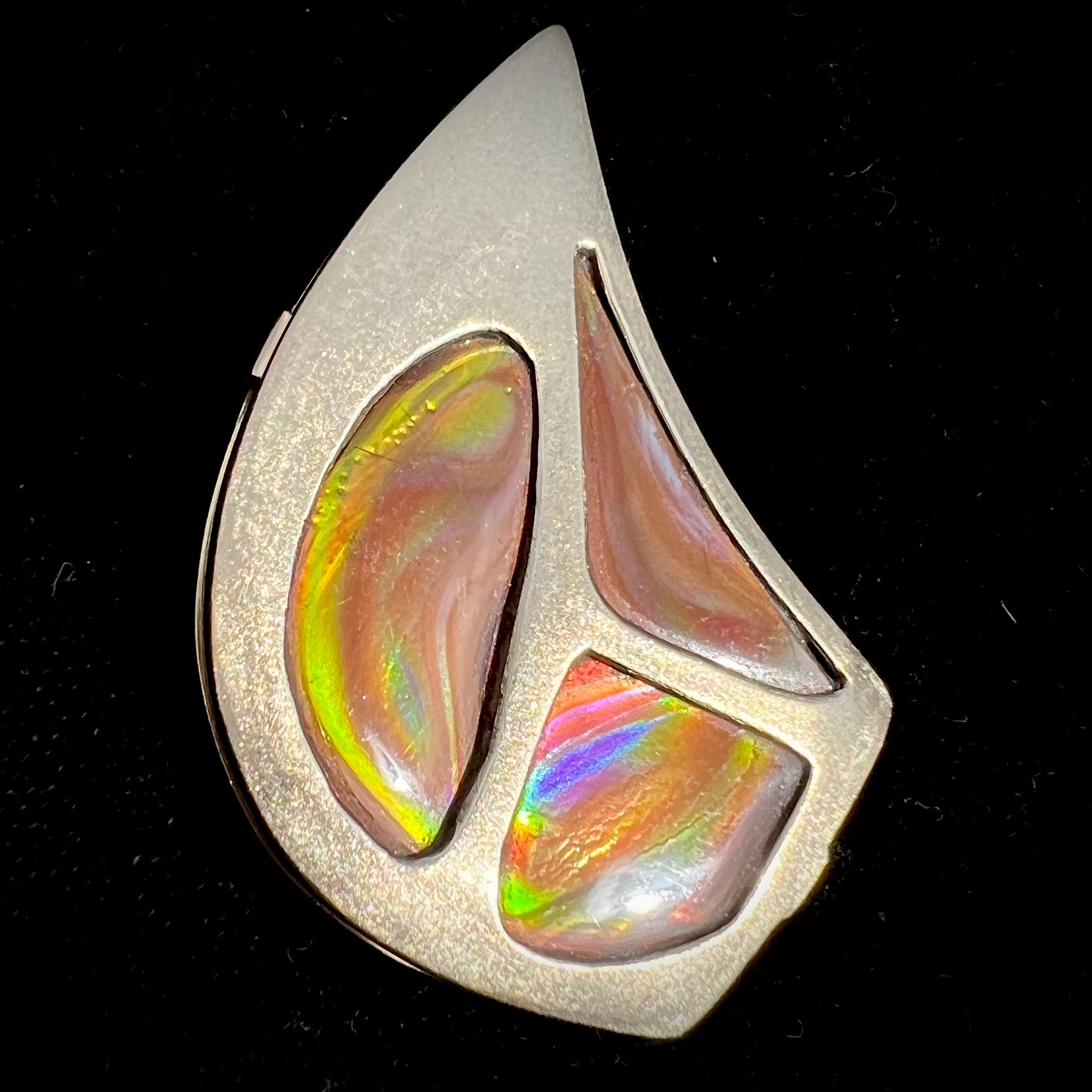 A men's gold pendant set with three fire agate stones.  The fire agate resembles an oil slick puddle.