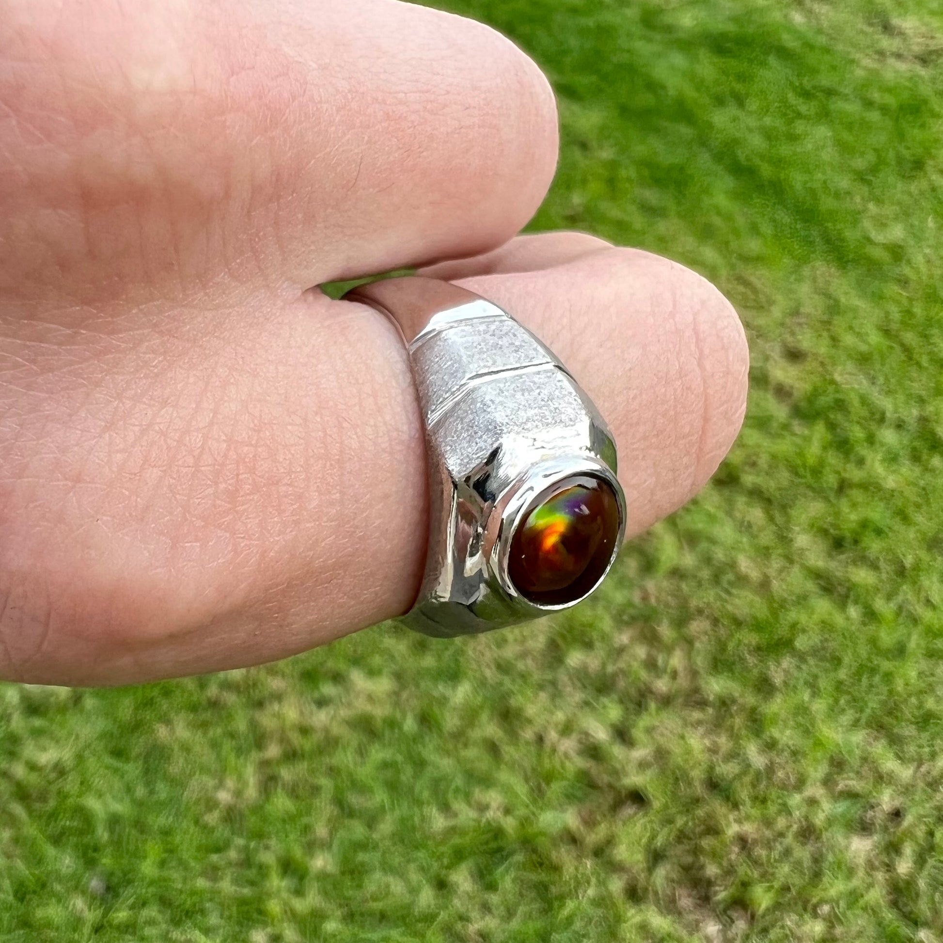 A round cabochon cut red and green fire agate set in a brushed metal white gold men's ring.