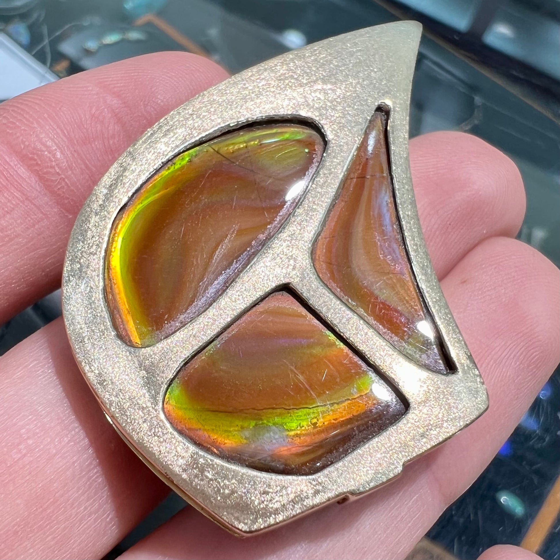 A men's gold pendant set with three fire agate stones.  The fire agate resembles an oil slick puddle.