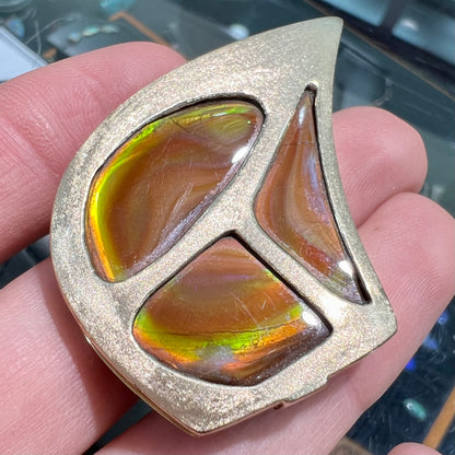 A men's gold pendant set with three fire agate stones.  The fire agate resembles an oil slick puddle.