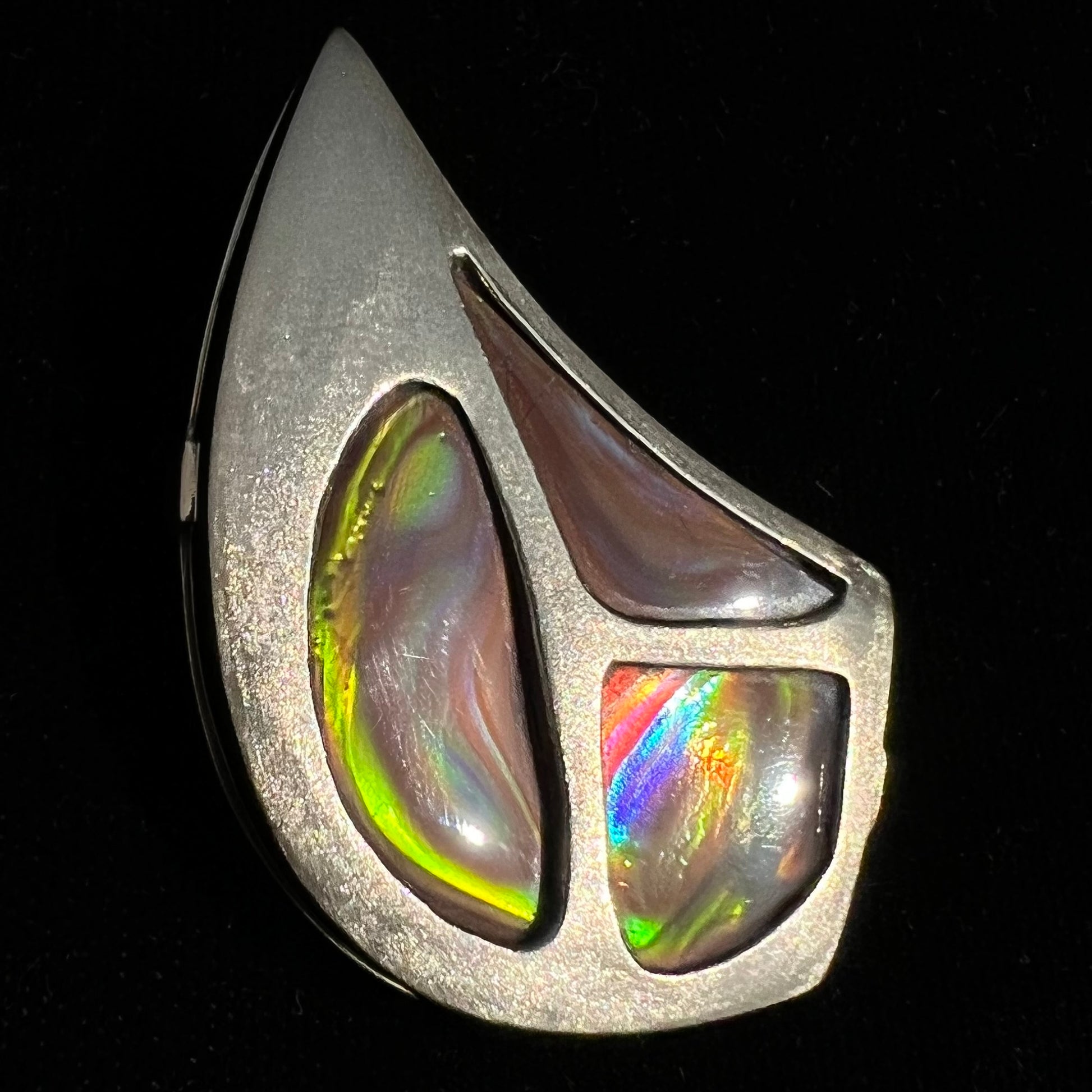 A men's gold pendant set with three fire agate stones.  The fire agate resembles an oil slick puddle.