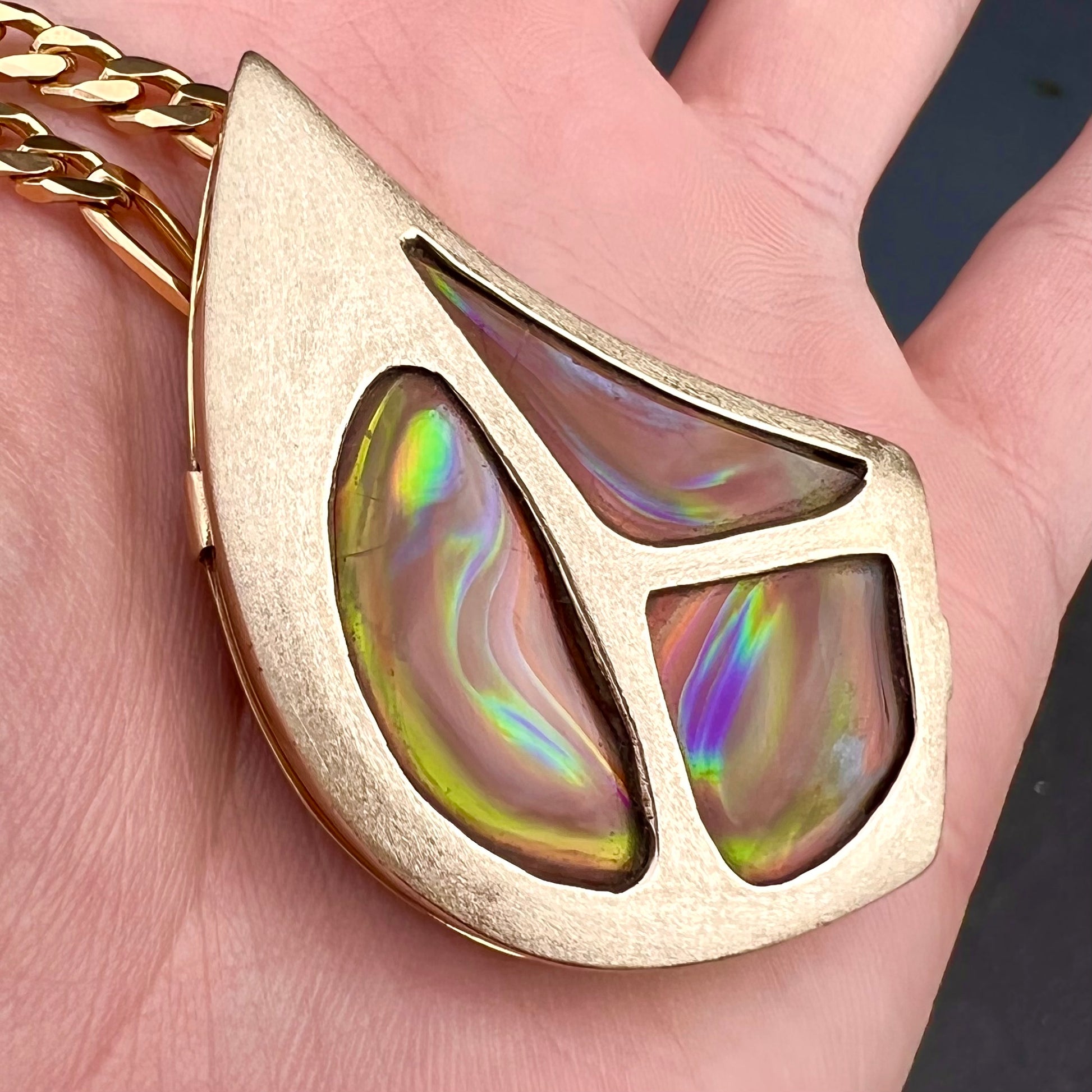 A men's gold pendant set with three fire agate stones.  The fire agate resembles an oil slick puddle.