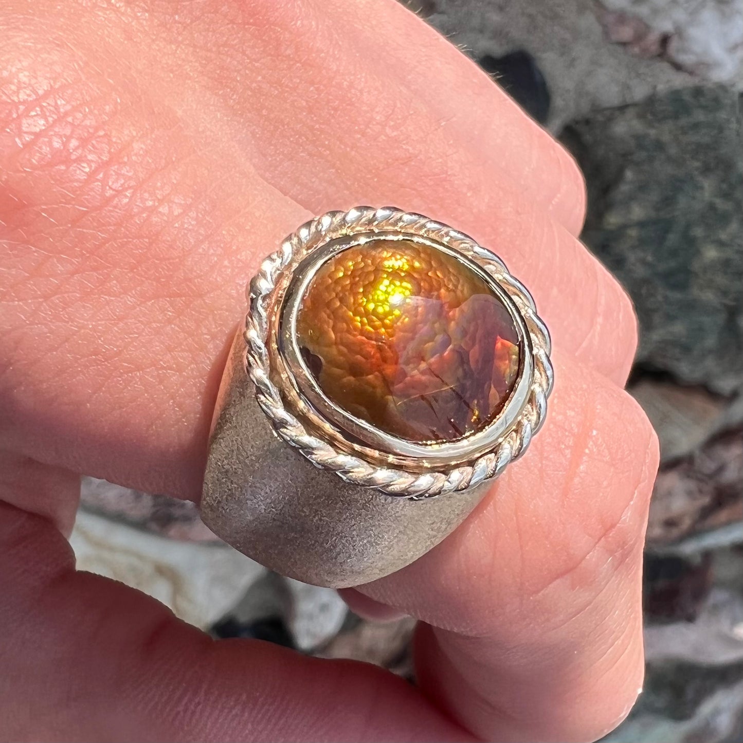 A men's matte finish textured gold fire agate ring.  There is a gold rope bezel around the oval cabochon cut stone.