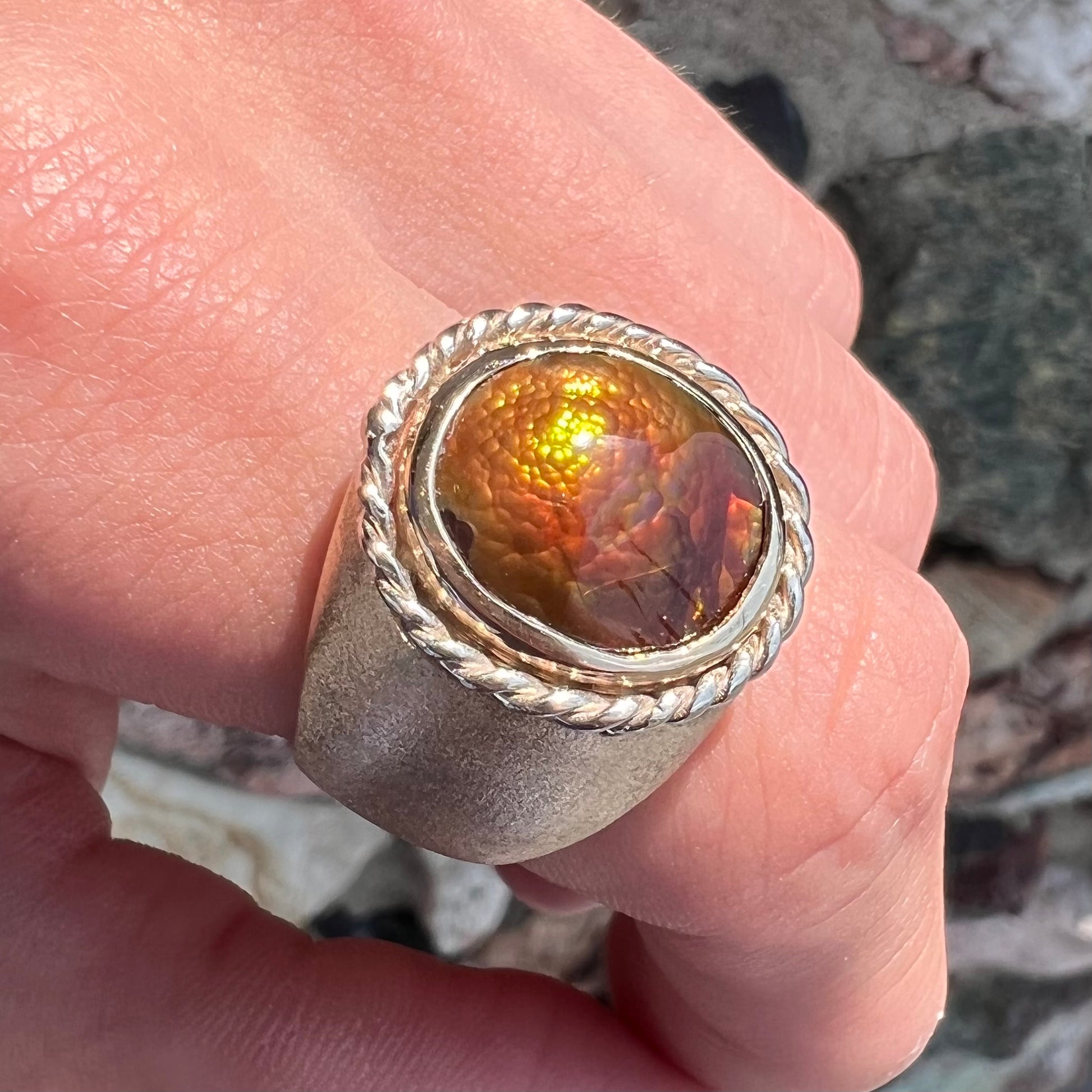 A men's matte finish textured gold fire agate ring.  There is a gold rope bezel around the oval cabochon cut stone.