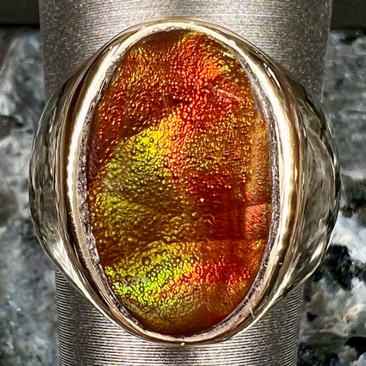 A yellow gold solitaire fire agate men's ring.  The fire agate is oval shape, and red and green in color.