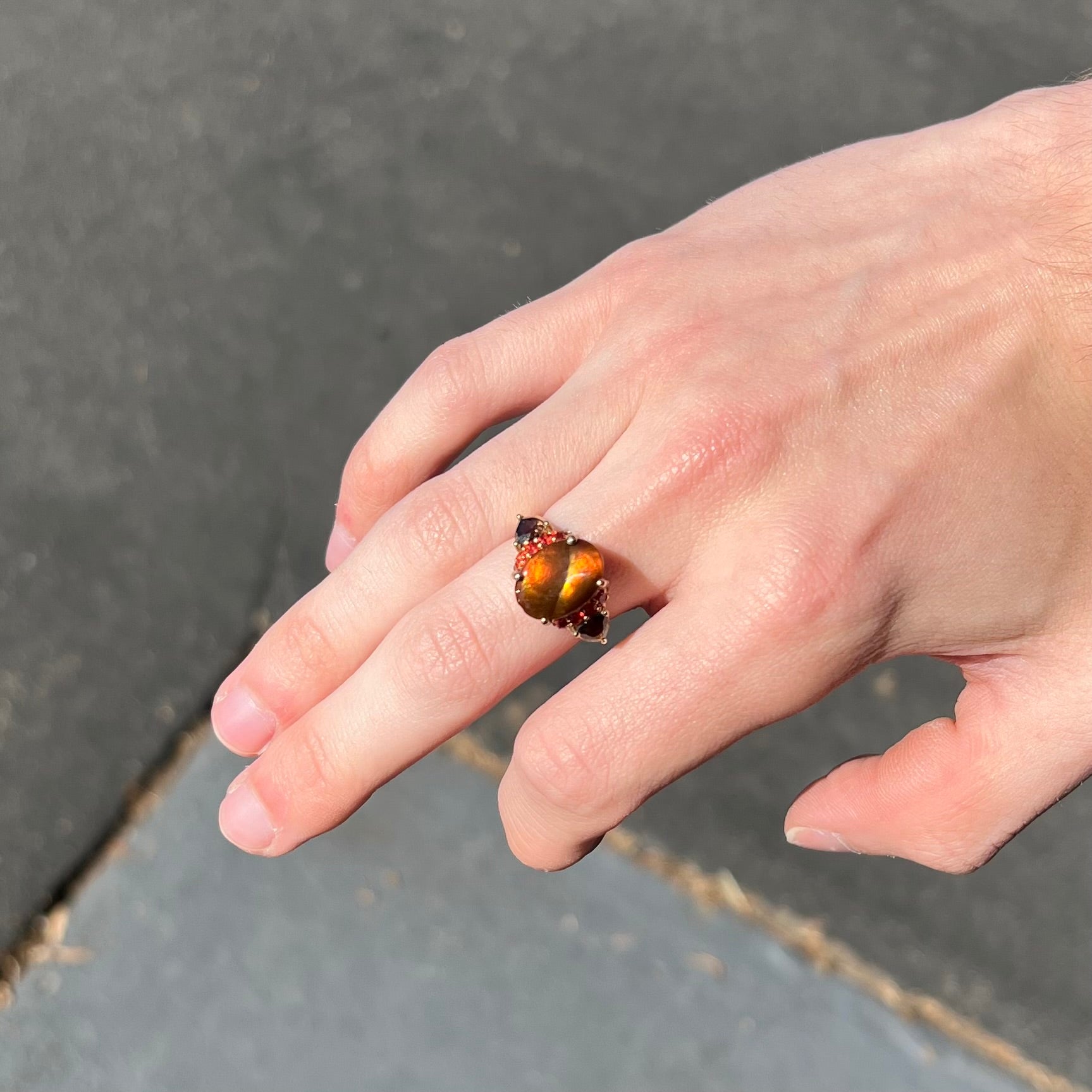 A ladies yellow gold fire agate ring set with trillion cut smoky quartz and round cut red-orange garnet accents.  The fire agate displays green and red.