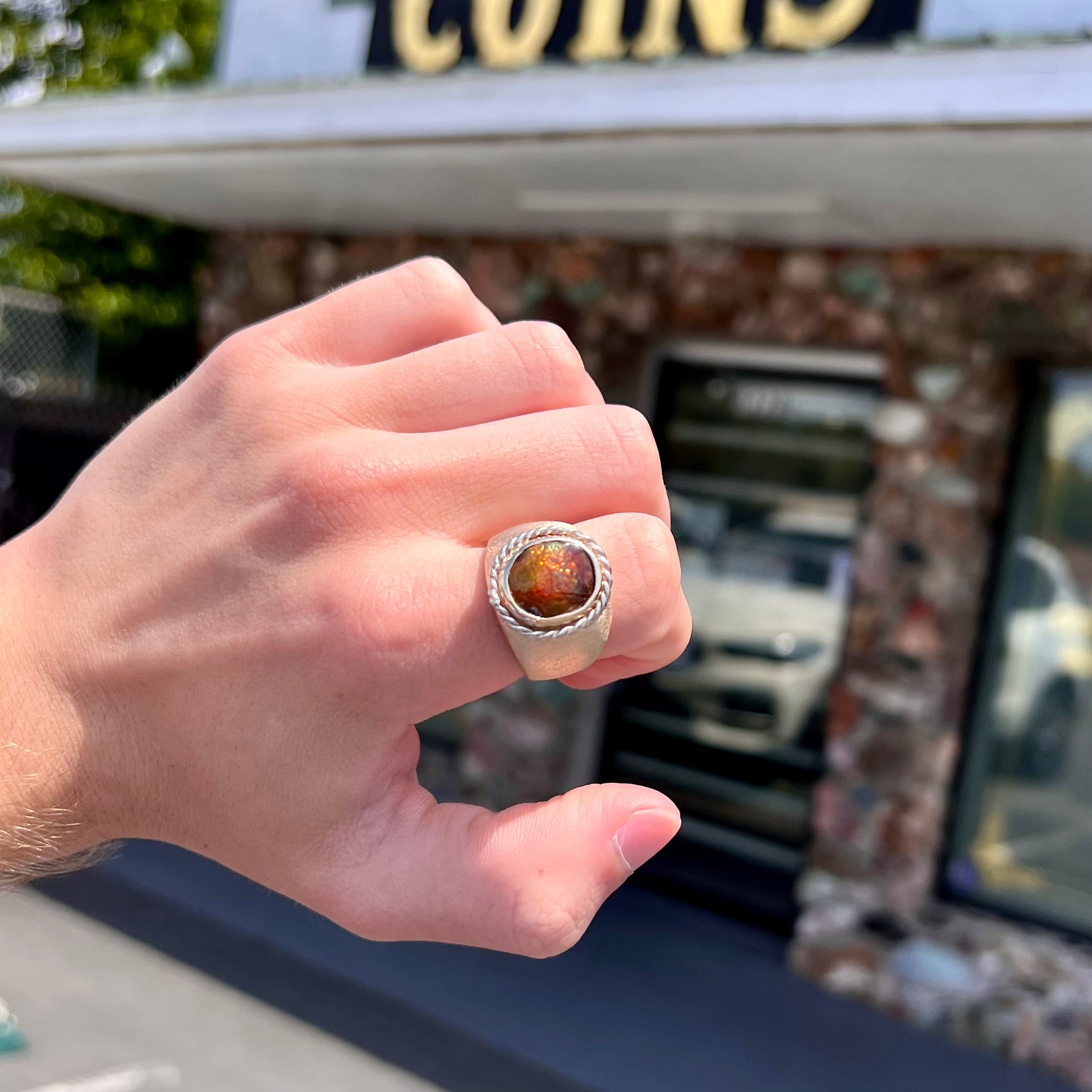 A men's matte finish textured gold fire agate ring.  There is a gold rope bezel around the oval cabochon cut stone.