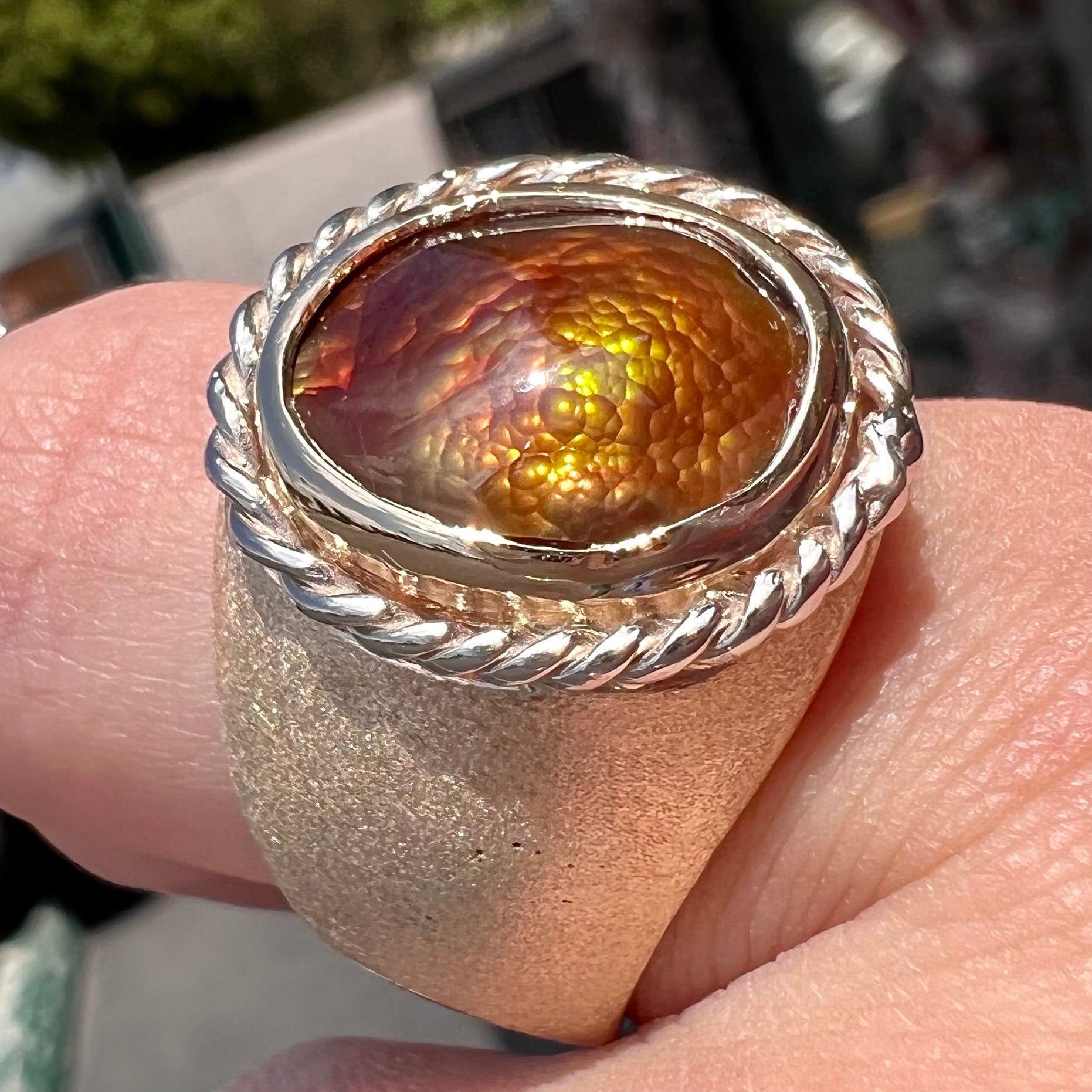 A men's matte finish textured gold fire agate ring.  There is a gold rope bezel around the oval cabochon cut stone.