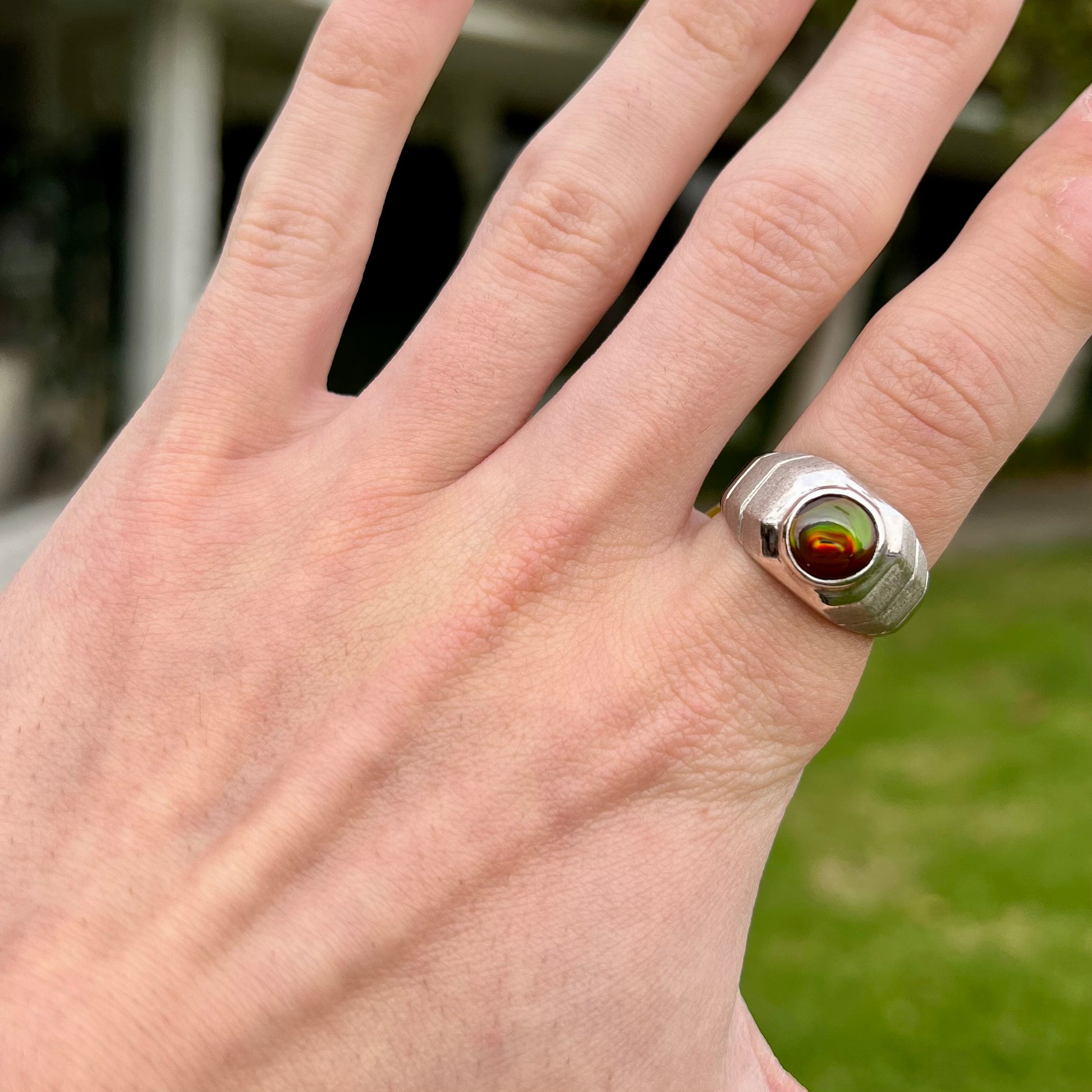 A round cabochon cut red and green fire agate set in a brushed metal white gold men's ring.