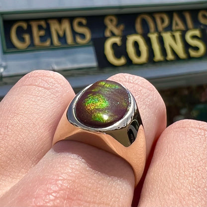 A yellow gold solitaire fire agate men's ring.  The fire agate is oval shape, and red and green in color.