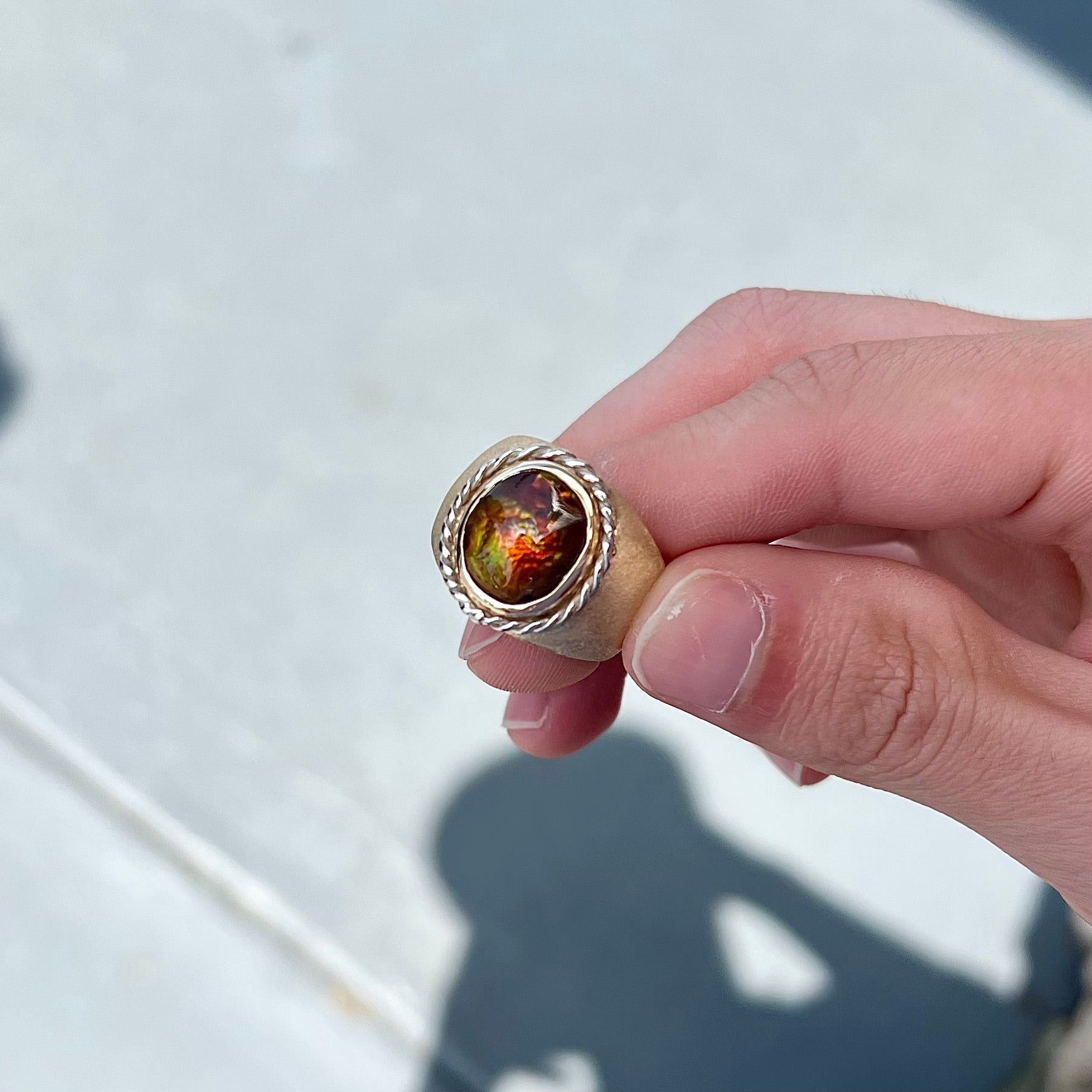 A men's matte finish textured gold fire agate ring.  There is a gold rope bezel around the oval cabochon cut stone.