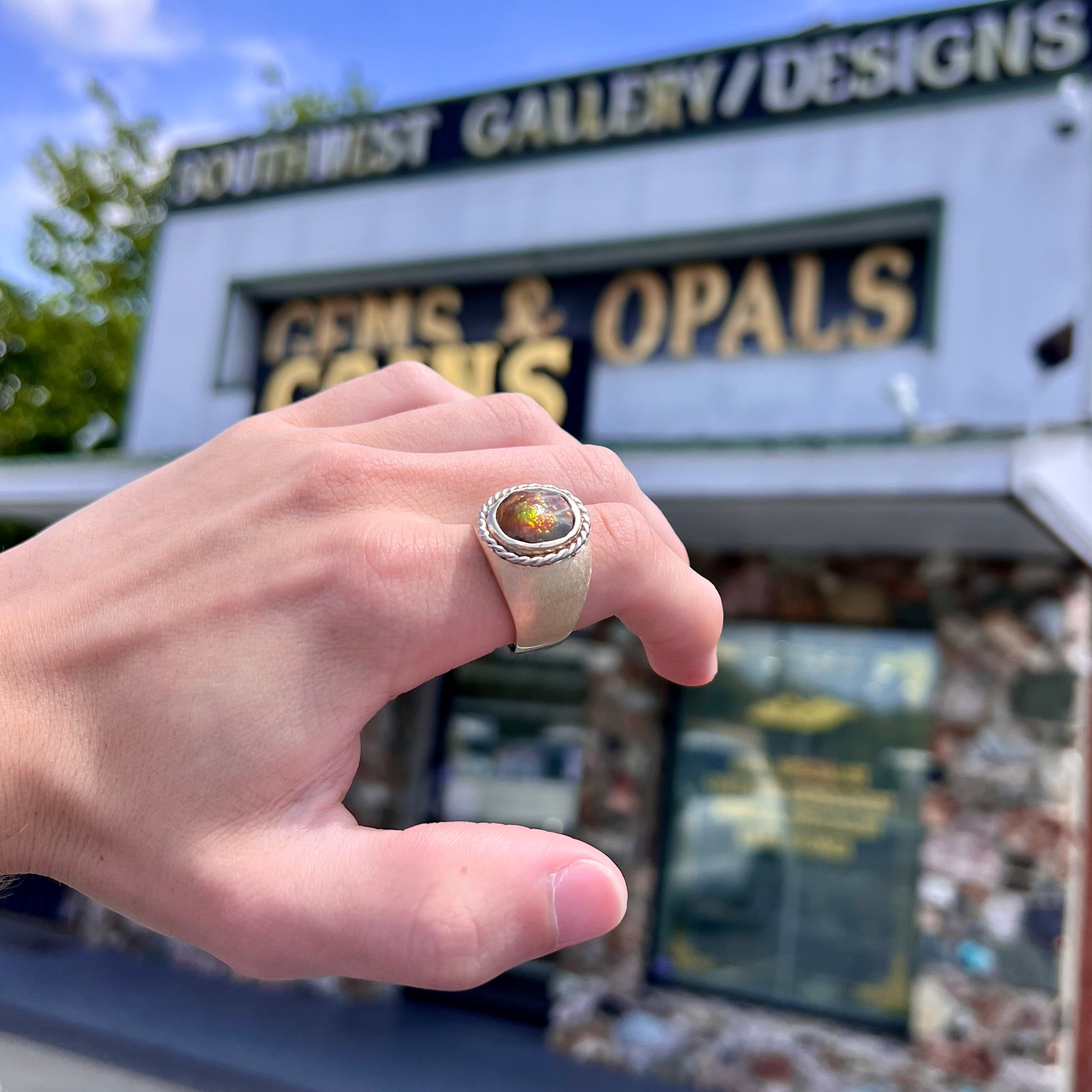 A men's matte finish textured gold fire agate ring.  There is a gold rope bezel around the oval cabochon cut stone.