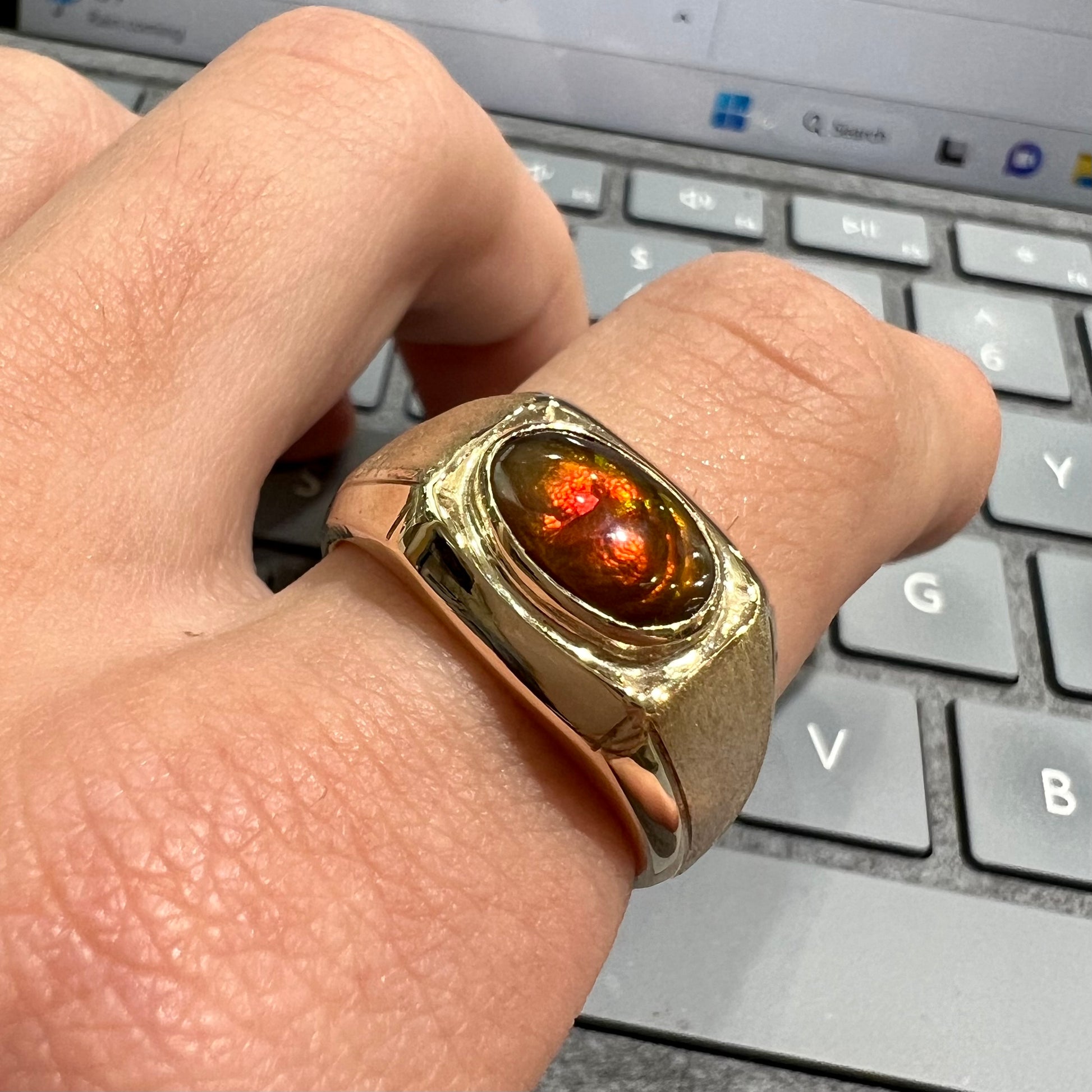 A yellow gold men's fire agate solitaire ring.  The fire agate is red with green undertones.