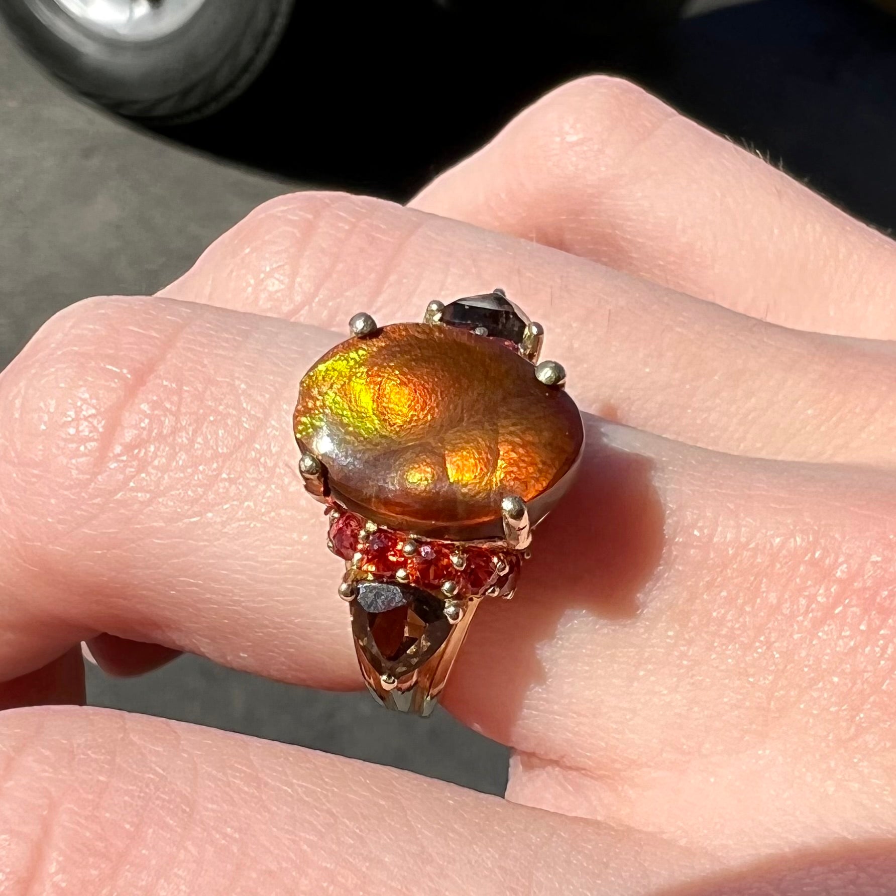 A ladies yellow gold fire agate ring set with trillion cut smoky quartz and round cut red-orange garnet accents.  The fire agate displays green and red.