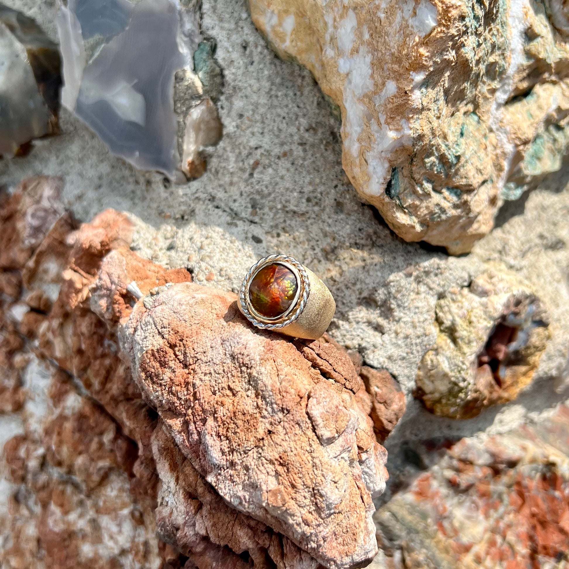 A men's matte finish textured gold fire agate ring.  There is a gold rope bezel around the oval cabochon cut stone.