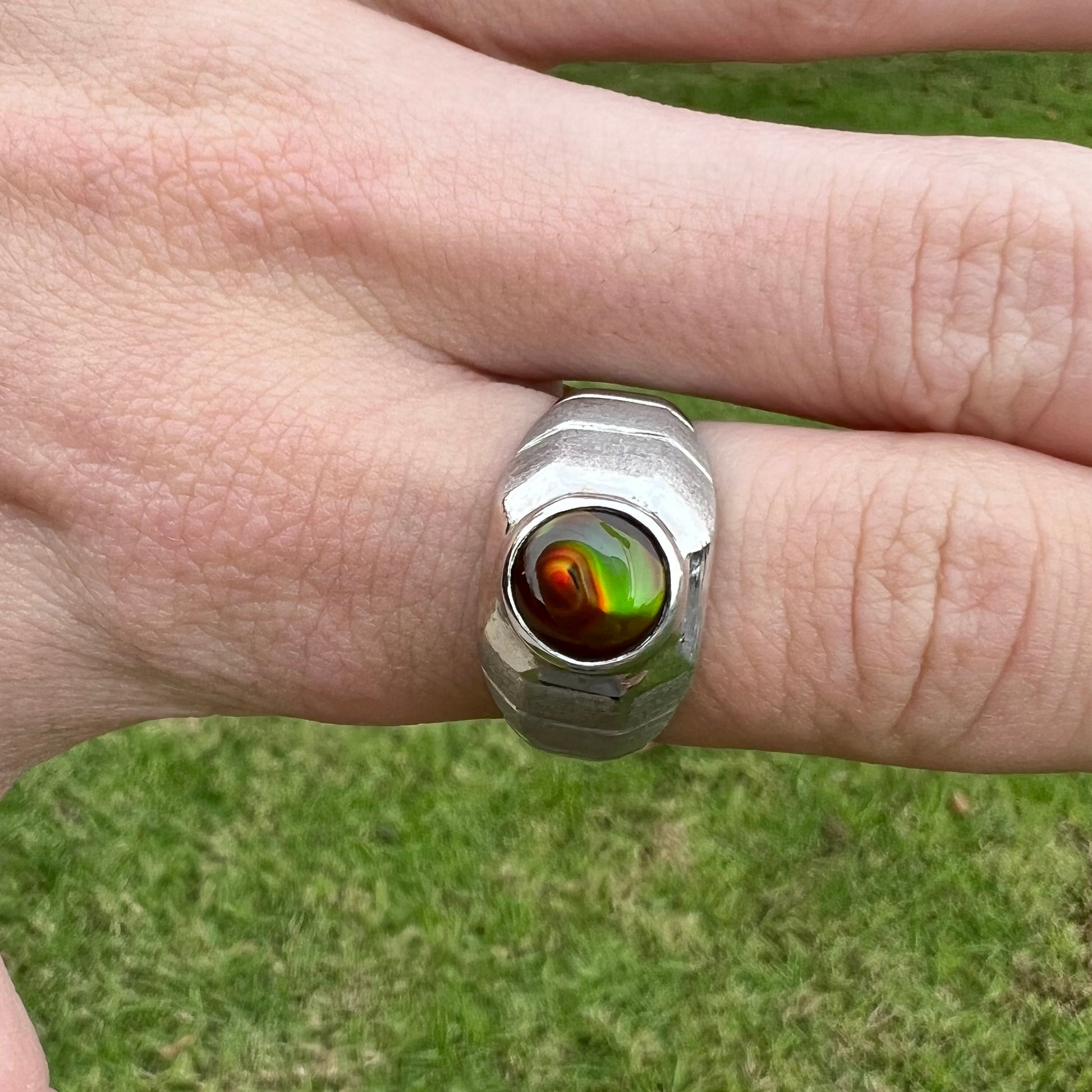 A round cabochon cut red and green fire agate set in a brushed metal white gold men's ring.