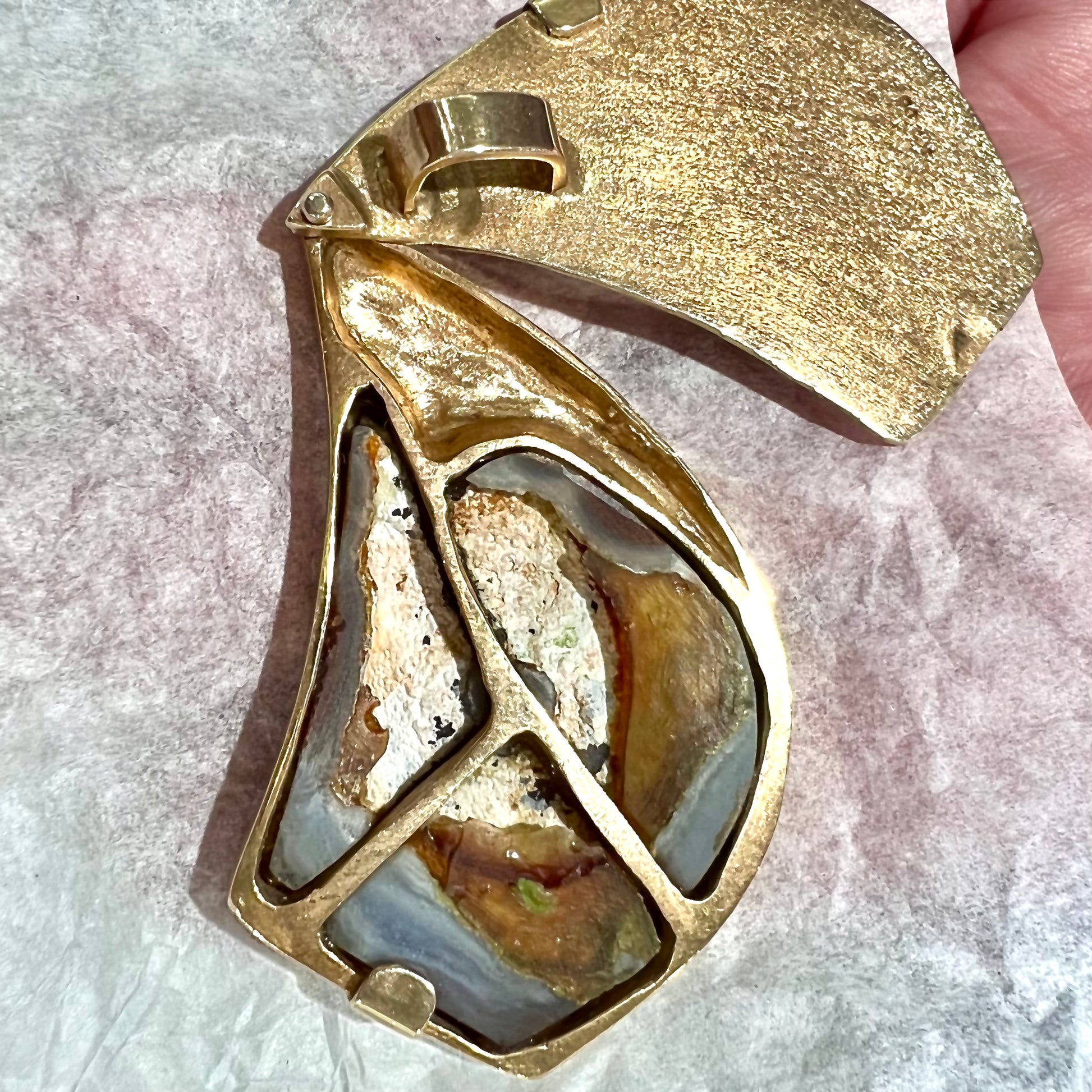 A men's gold pendant set with three fire agate stones.  The fire agate resembles an oil slick puddle.