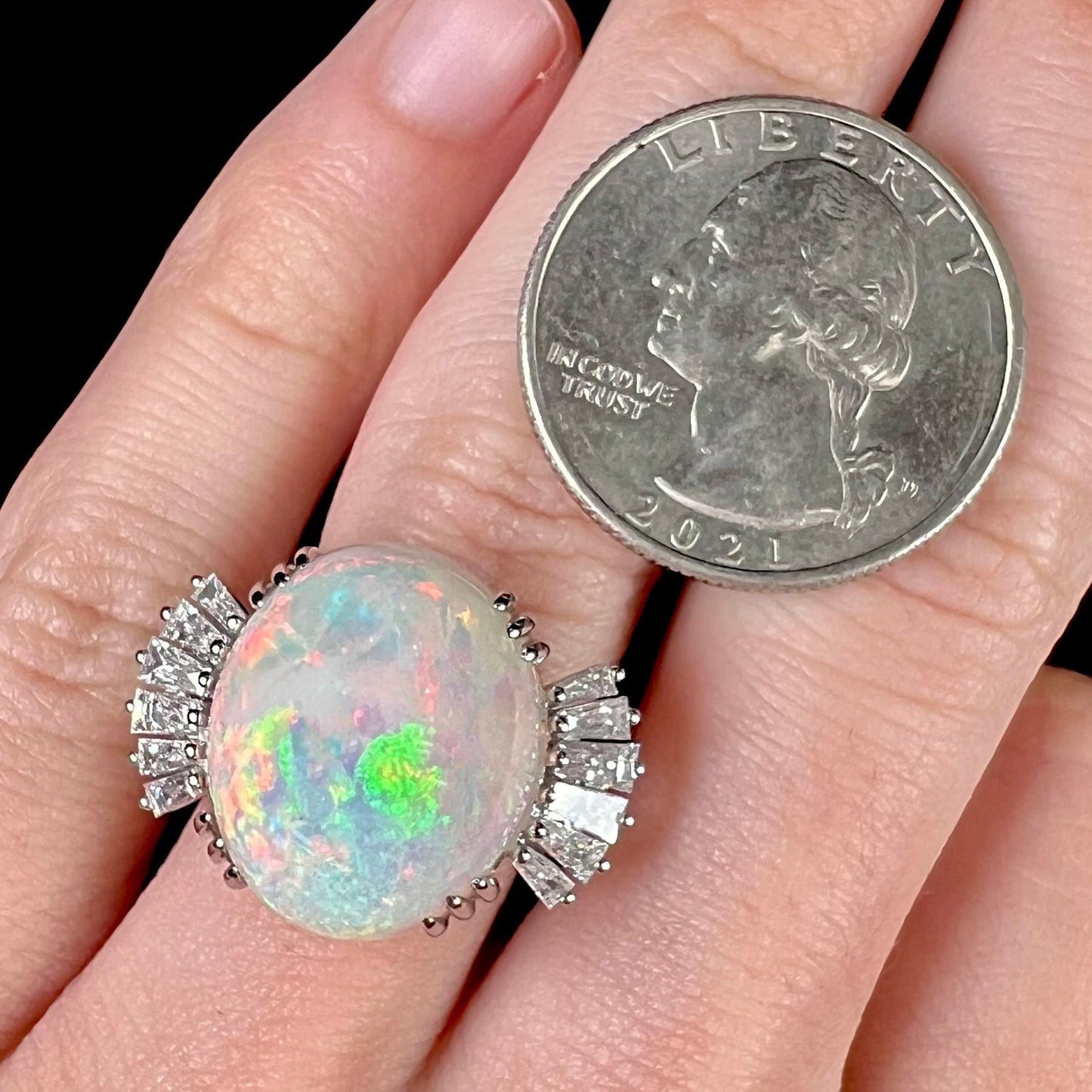 An oval cabochon cut opal mounted in a ladies' white gold ring between tapered baguette cut diamonds.